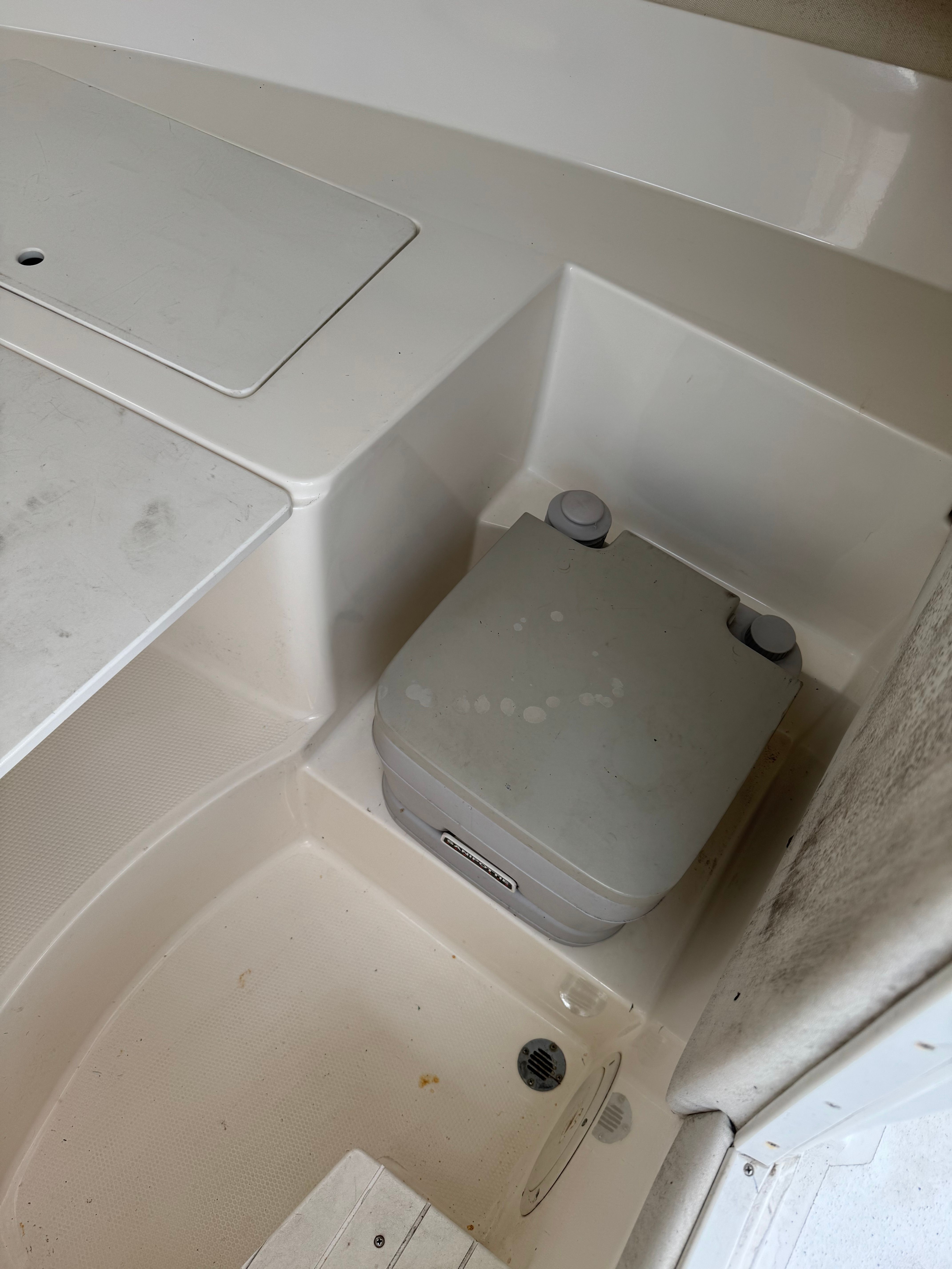 A portable toilet system is installed in a boat, surrounded by white surfaces.
