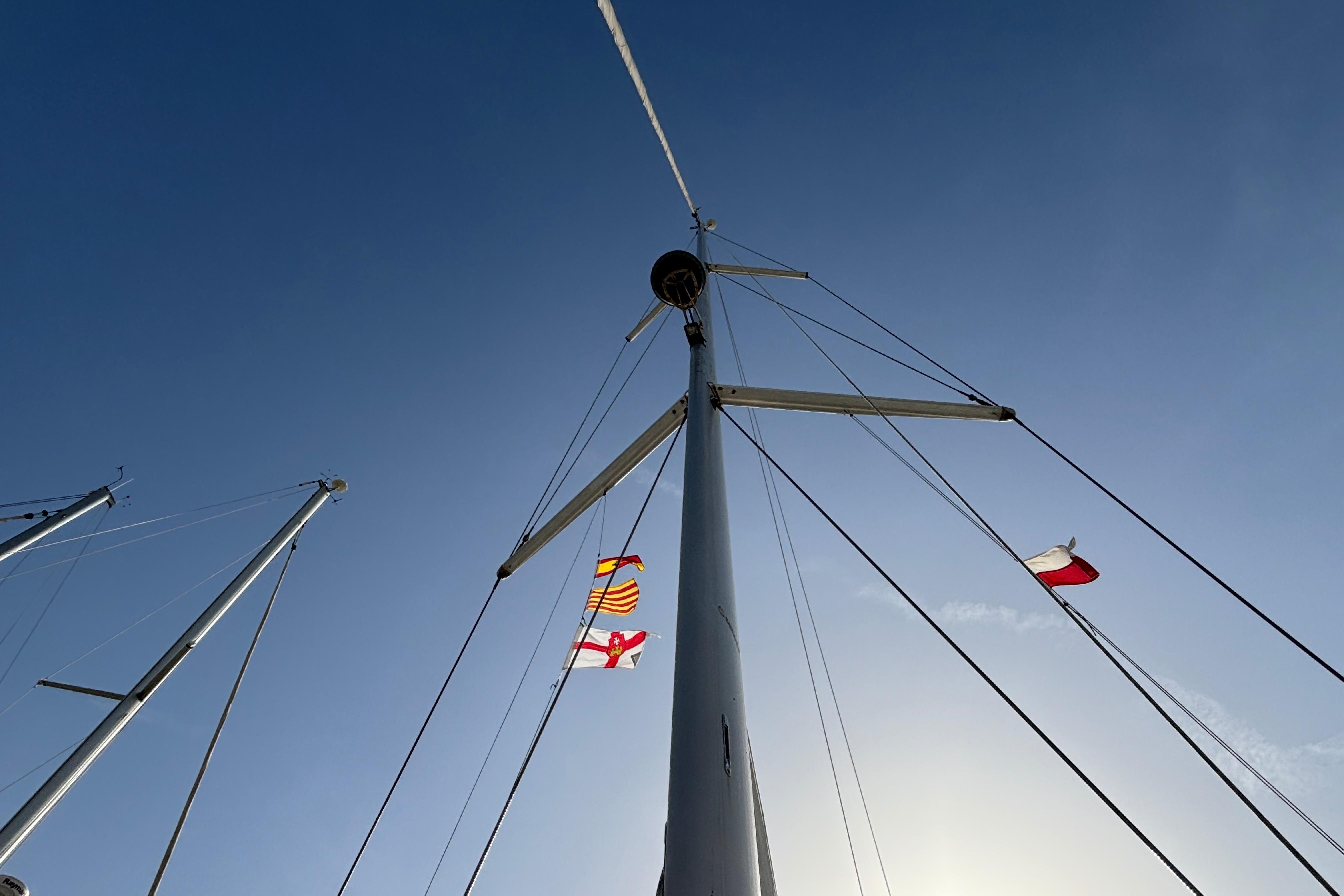 Mast of 2010 Bavaria Cruiser 55 sailboat with flags against clear blue sky.