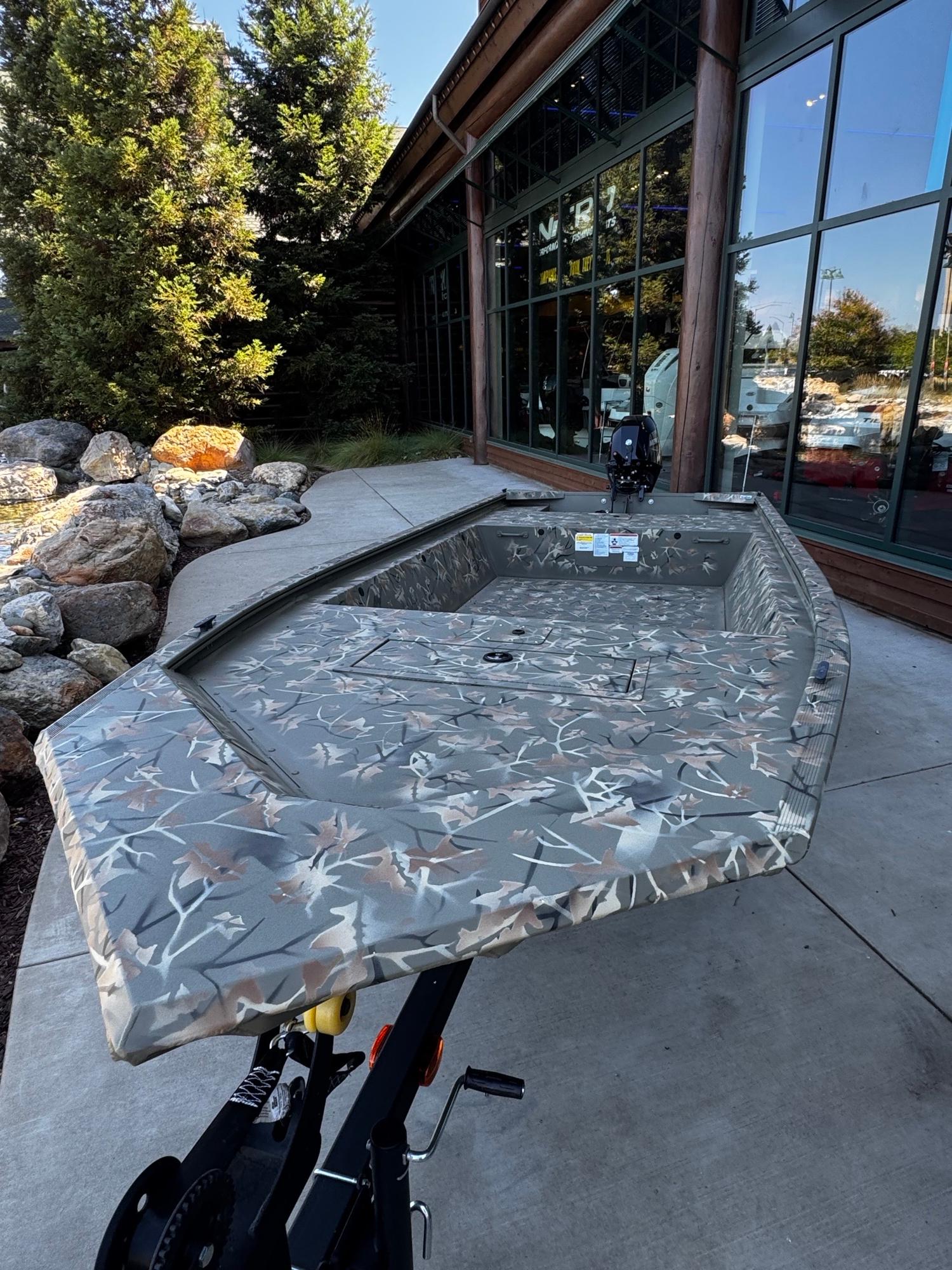 2025 Tracker Grizzly 1648 Jon boat with camouflage design, displayed outdoors near a building.