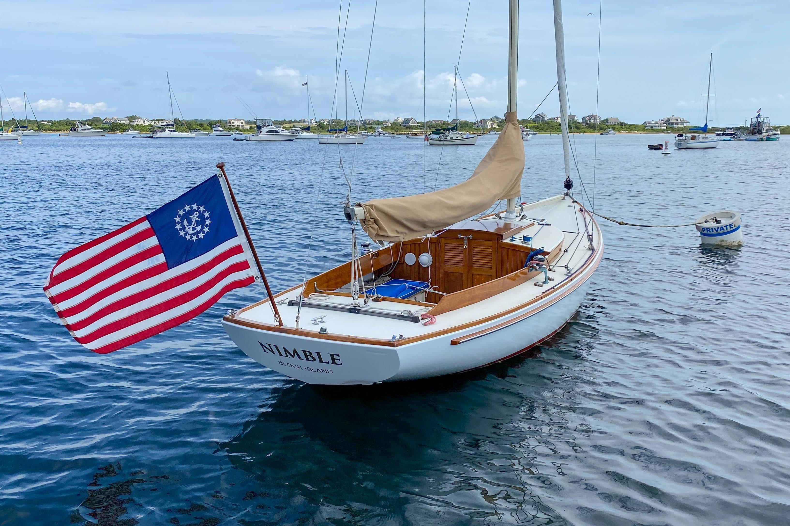 2003 Herreshoff Alerion 26 sailboat named Nimble on calm water, displaying a historical American flag.