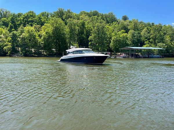 2019 Tiara Yachts C53 cruising on a serene lake with lush green trees.