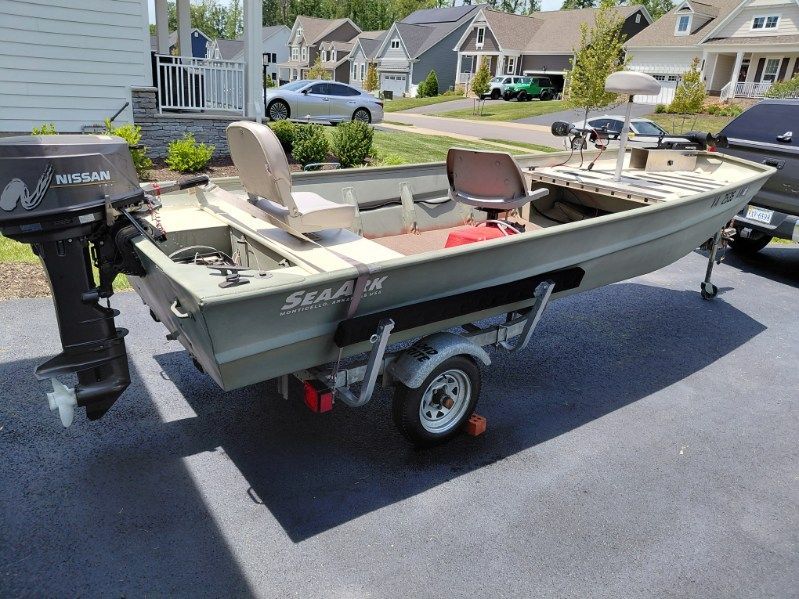 A 1999 SeaArk jon boat on a trailer in a residential area. It features a Nissan outboard motor.