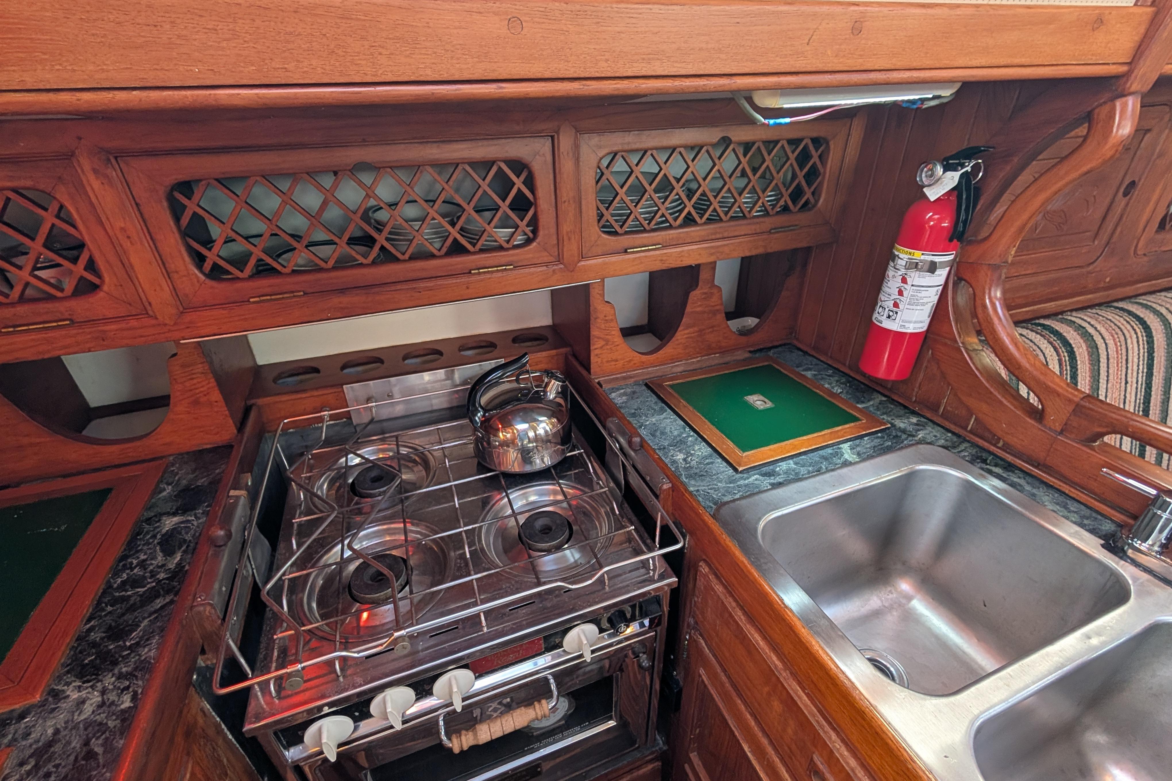 Vintage 1983 Robert Perry 41 yacht kitchen with stove, sink, and fire extinguisher.