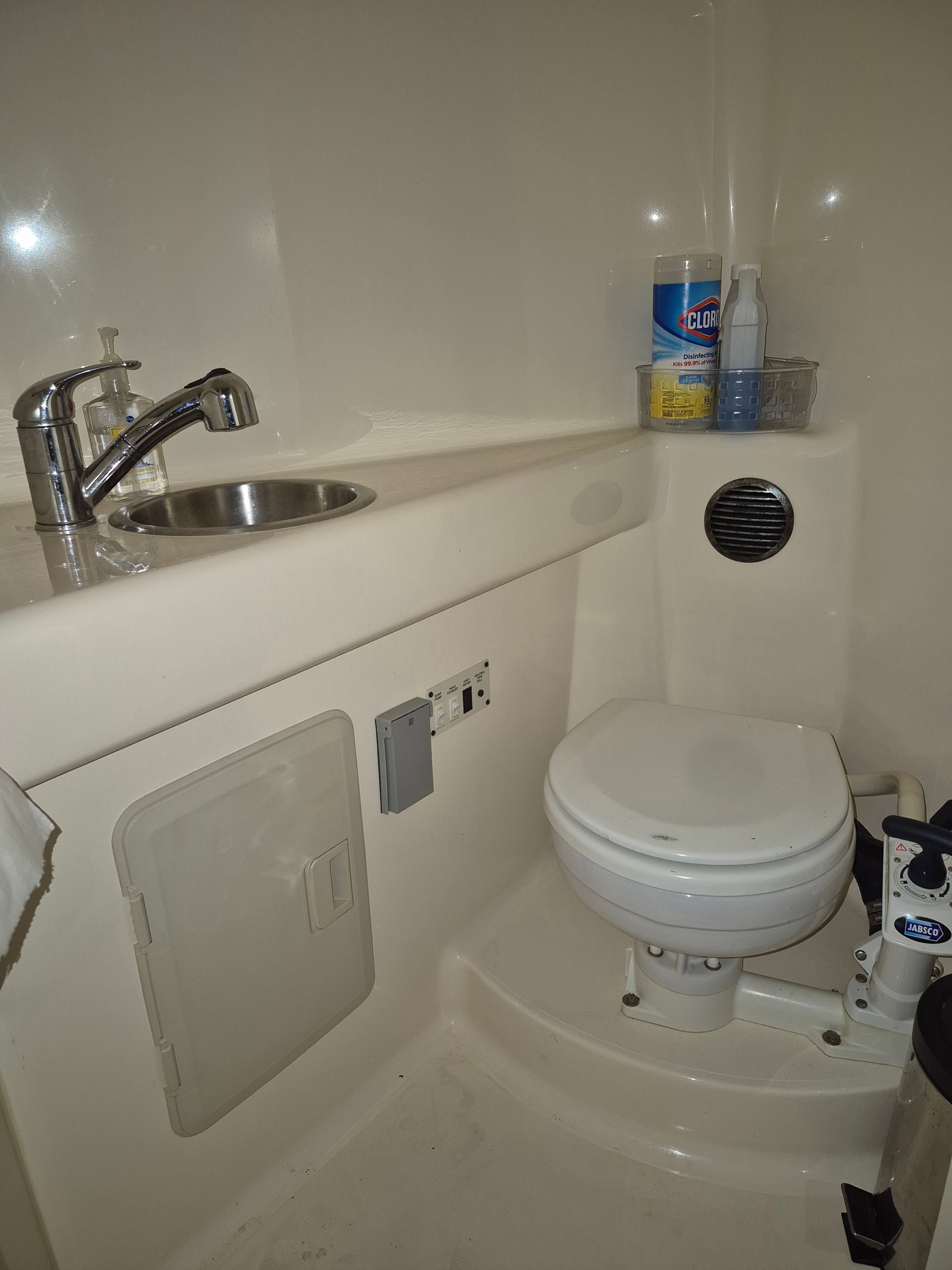 Interior view of a boat bathroom with sink, toilet, and cleaning supplies.