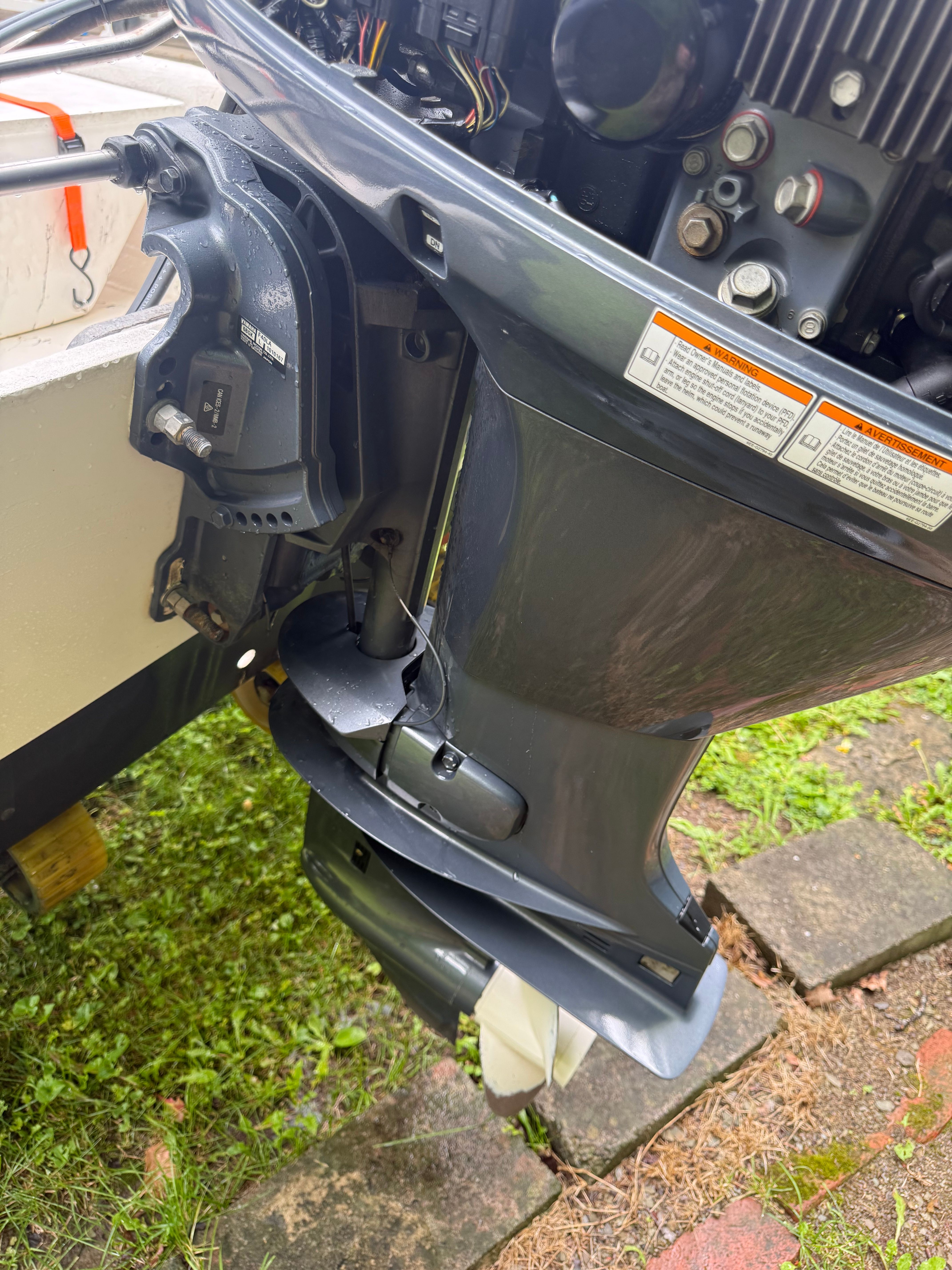 Close-up of an outboard motor on a boat, surrounded by grass and stones.