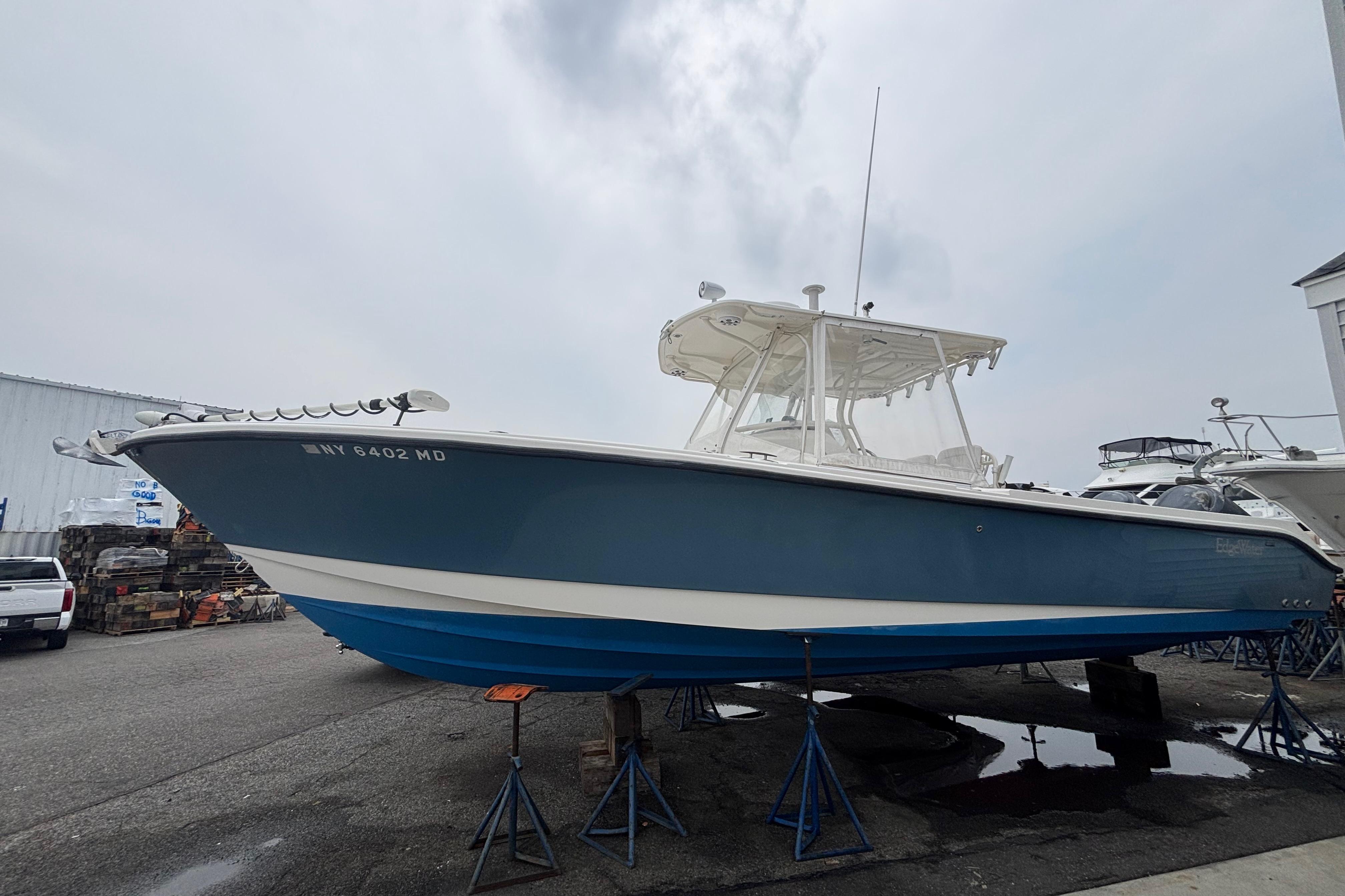 2006 Edgewater 318CC boat on stands, blue hull, overcast sky background.