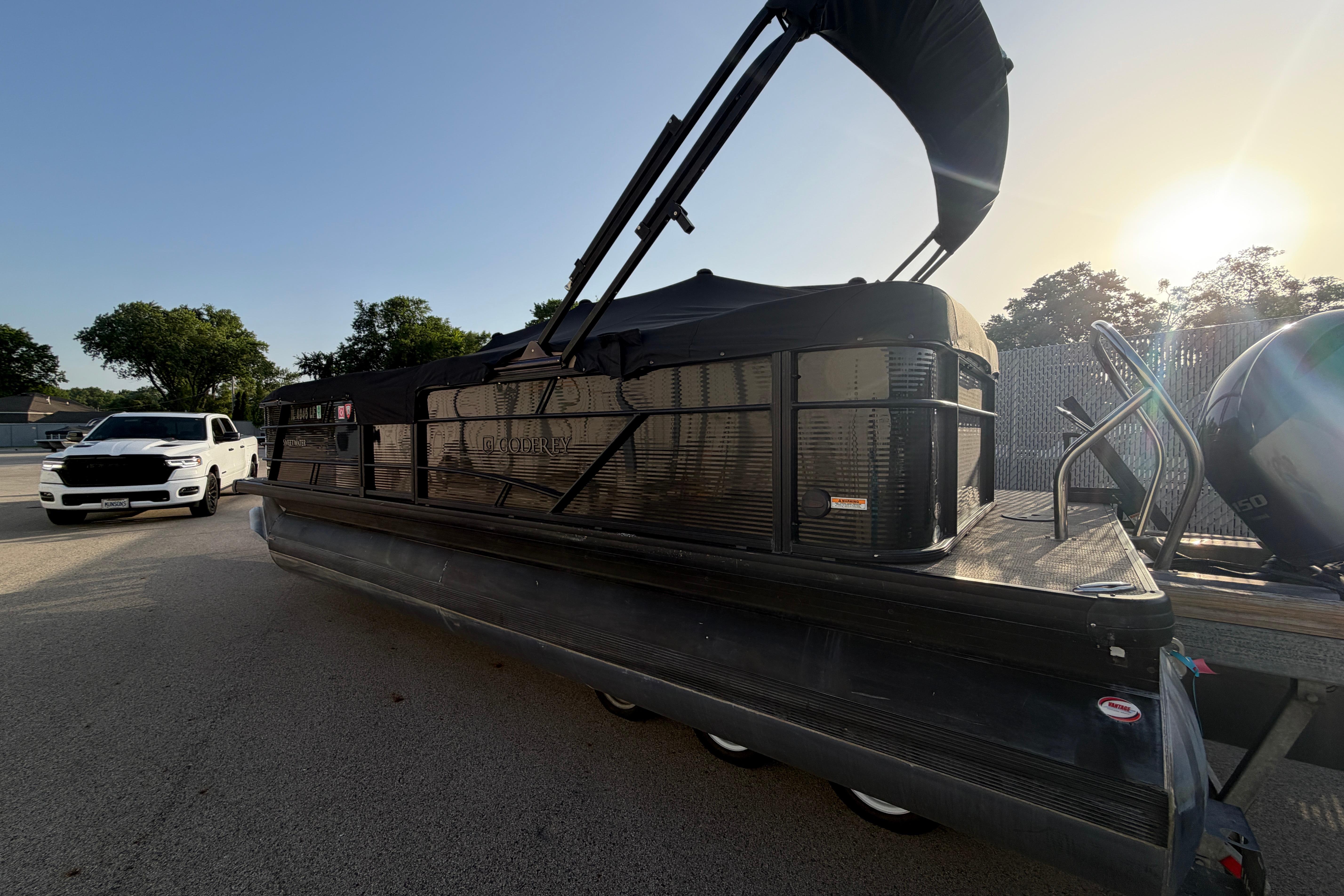 2023 Godfrey Sweetwater 2286 C pontoon boat with canopy, parked beside a white vehicle.