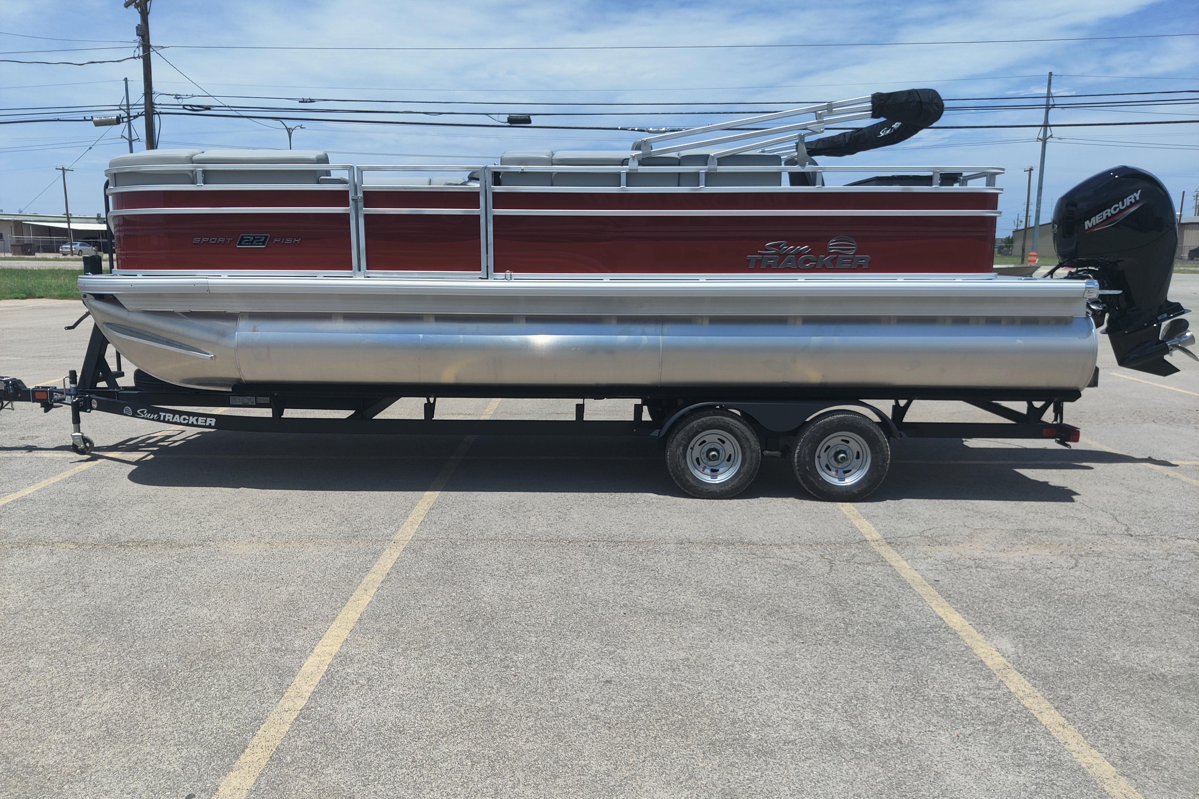 2026 Sun Tracker SportFish 22 DLX pontoon boat on trailer in parking lot.