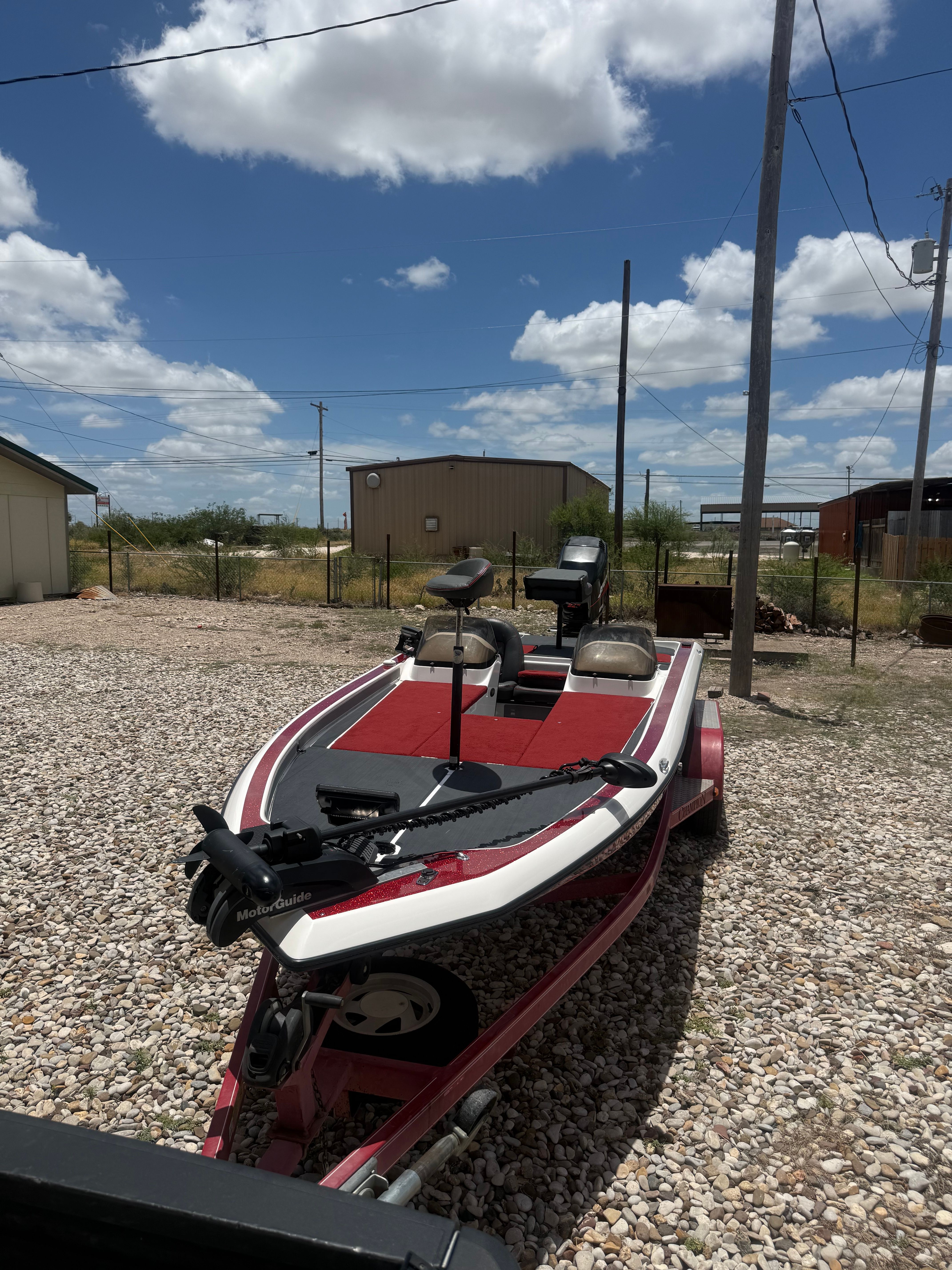 A 1999 Champion 202 boat on a trailer in a gravel lot under a blue sky.