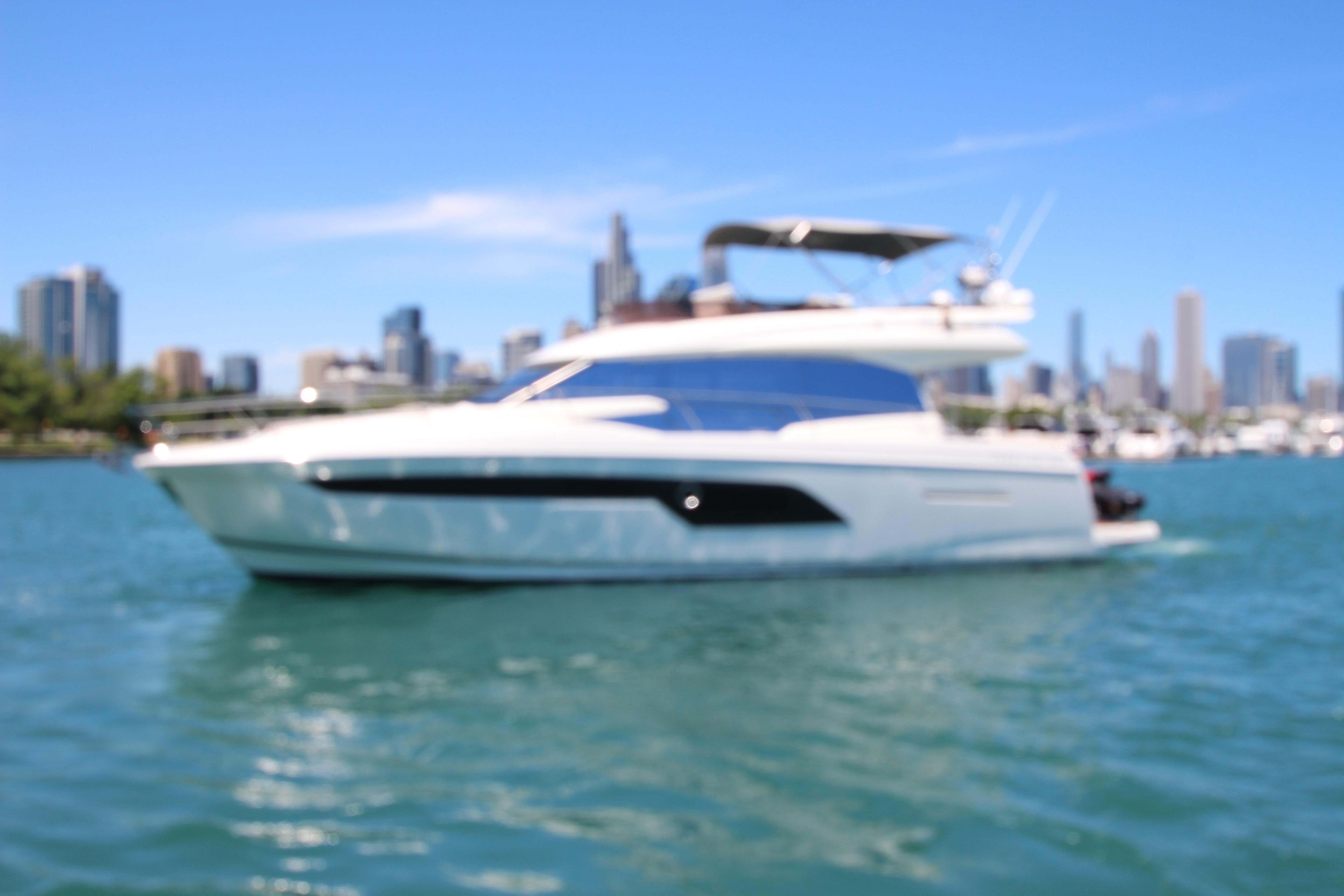 Blurry image of a 2022 Prestige 520 yacht on water with city skyline background.