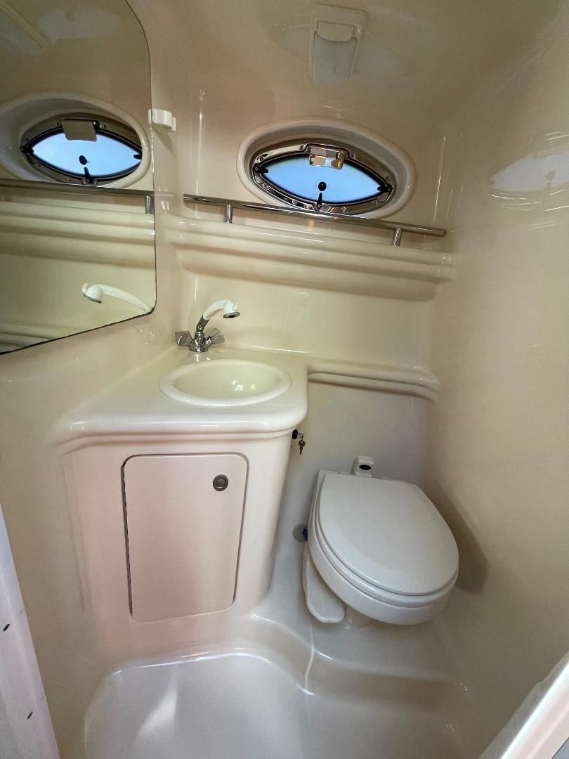 The image shows a compact bathroom with a sink, toilet, and porthole.