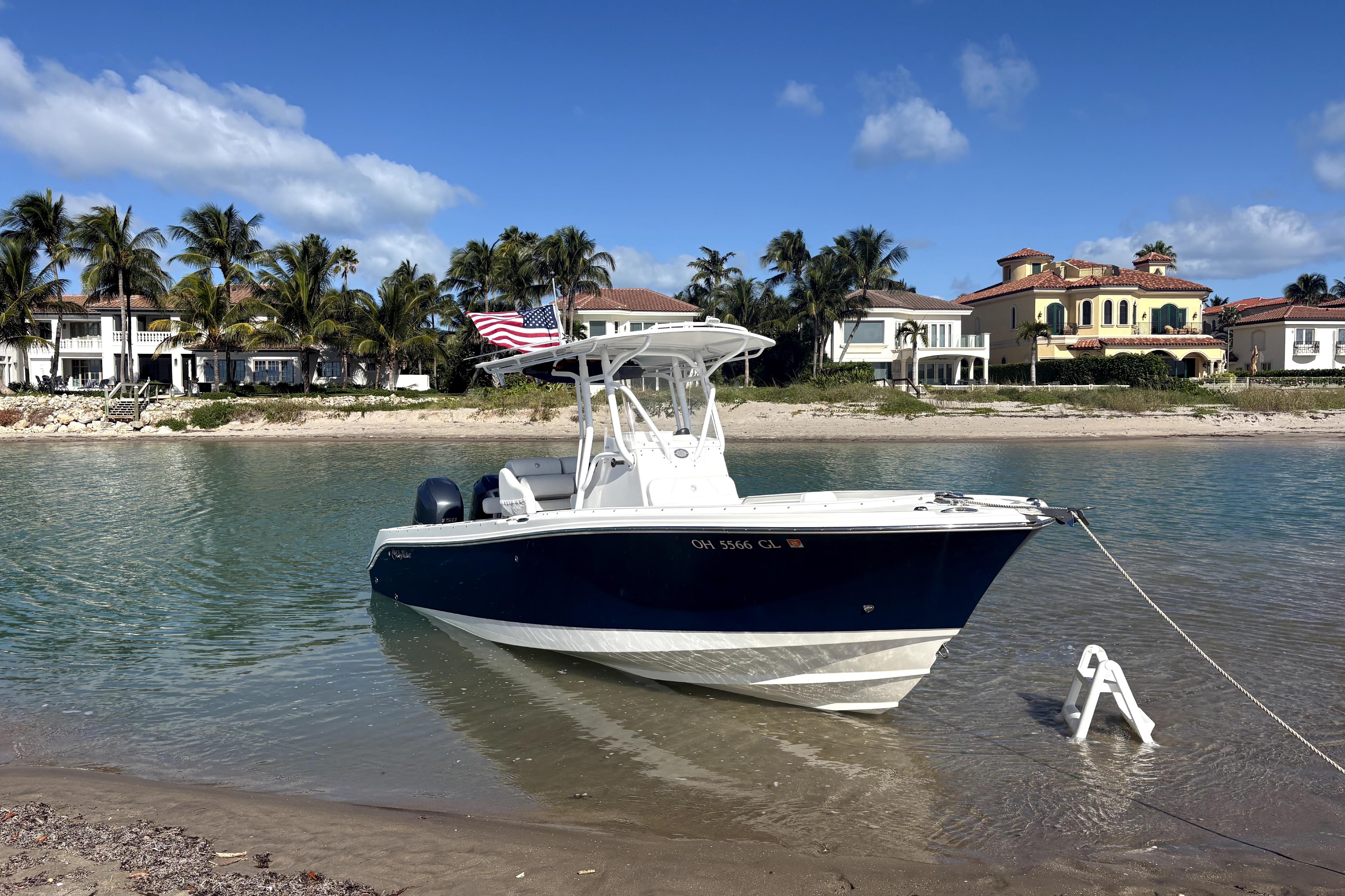 Edgewater 245CC 2015 boat anchored near a sandy beach with luxury homes and palm trees.