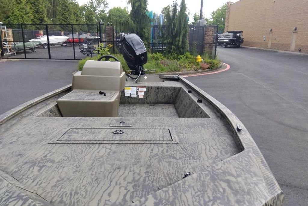 2026 Tracker Grizzly 1648 SC boat with camouflage design, parked outdoors near a fence.