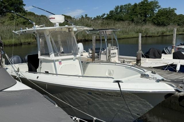 2006 Sailfish 2660 CC boat docked by a serene riverside with lush greenery.