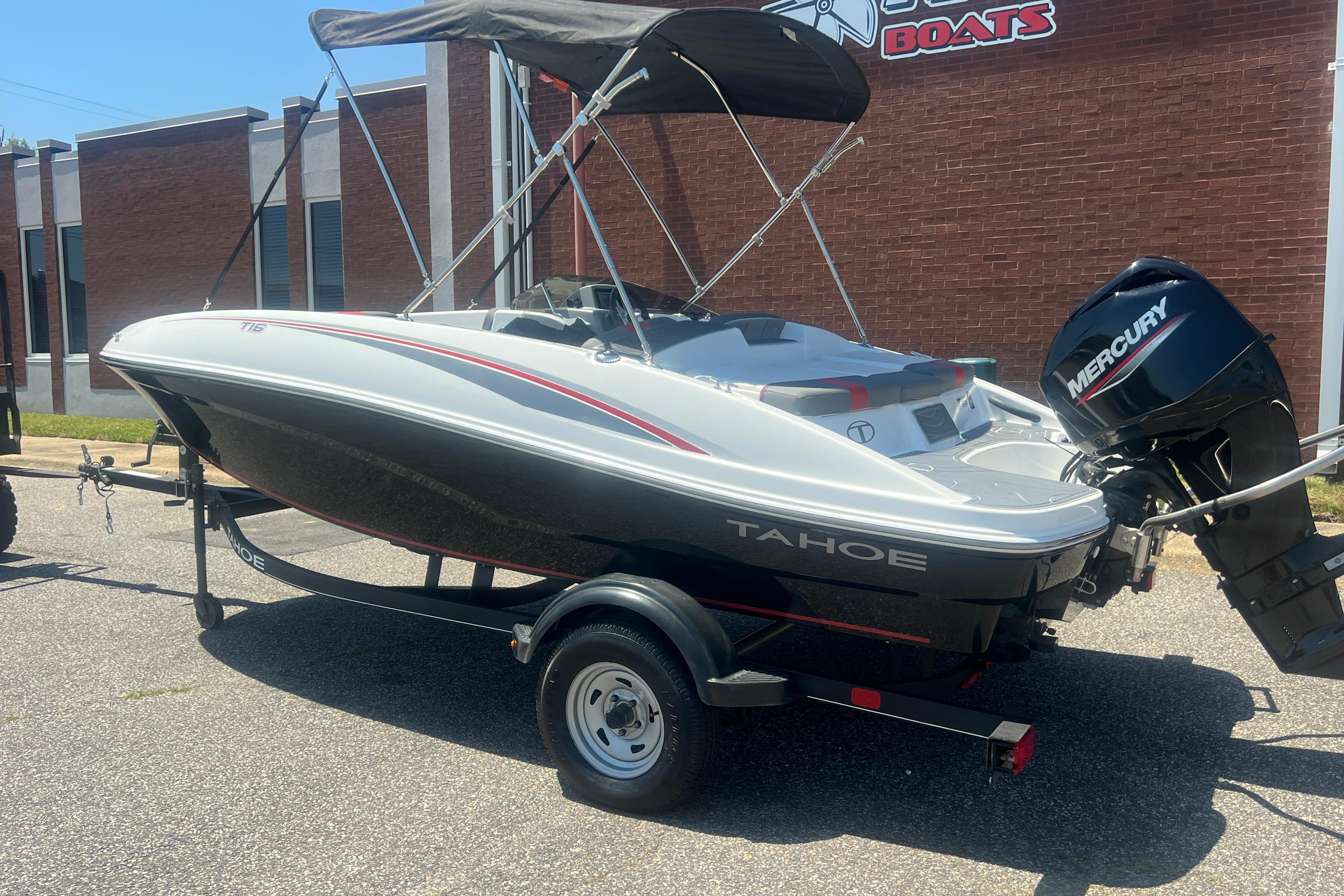 2023 Tahoe T16 boat with Mercury engine on trailer, parked outside a building.
