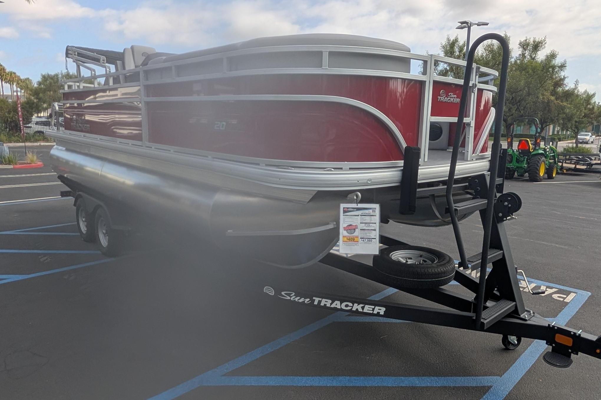 2026 Sun Tracker SportFish 20 DLX pontoon boat on trailer in parking lot.