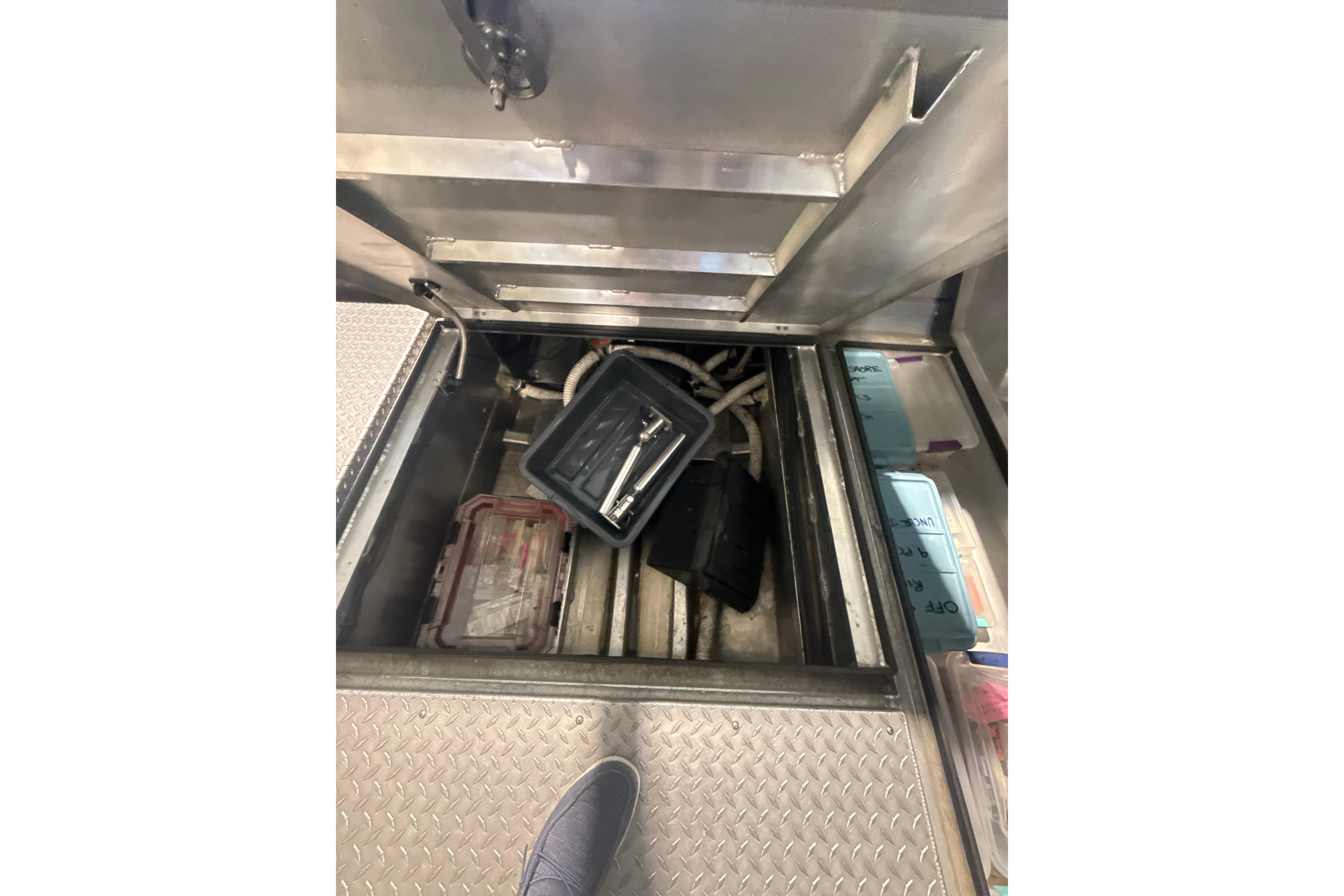 Open storage compartment in 2022 Hewescraft 270 Alaskan Hardtop boat, containing tools and equipment.