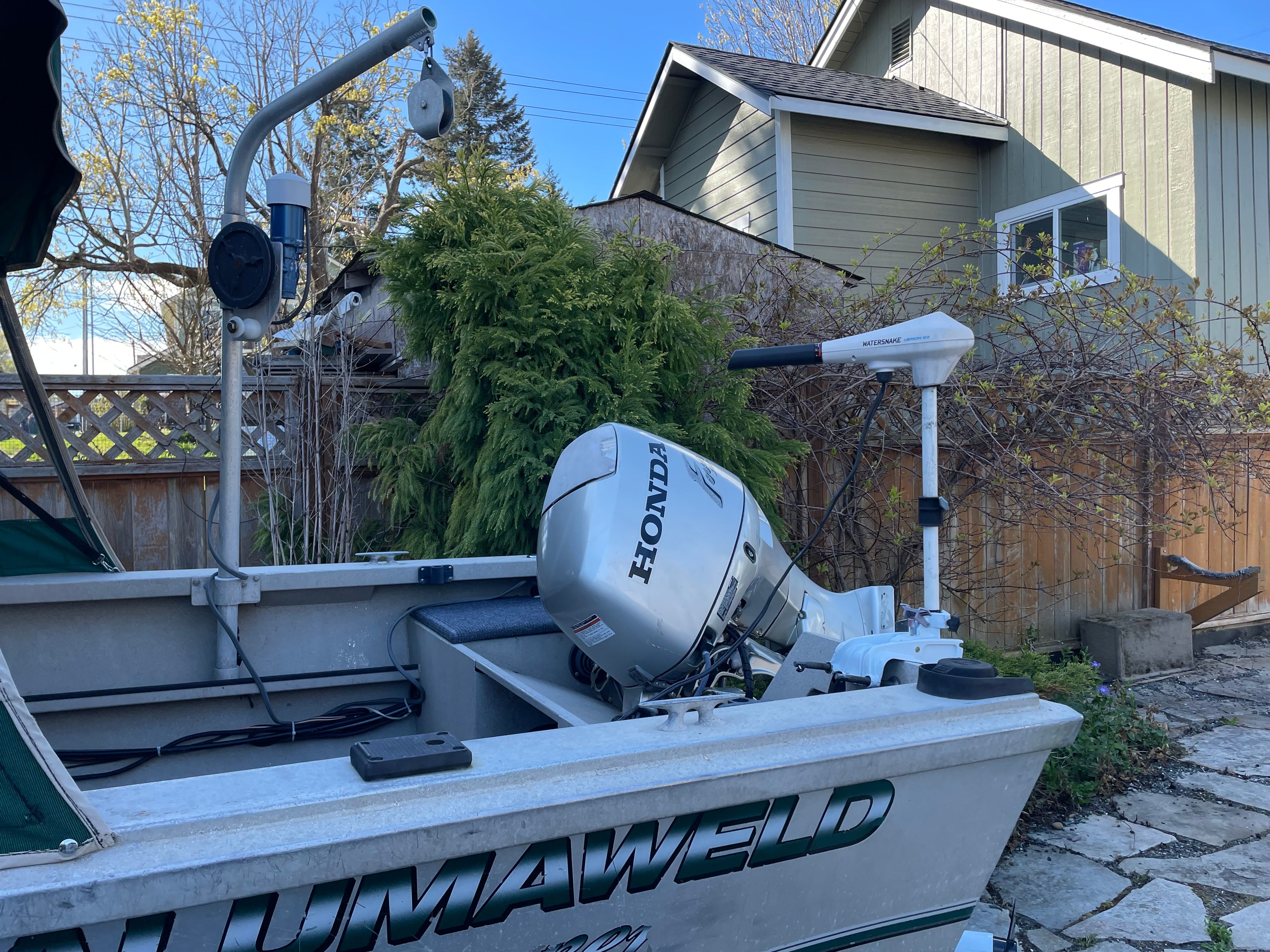 A 2001 Alumaweld Stryker boat with a Honda outboard motor, parked in a garden.