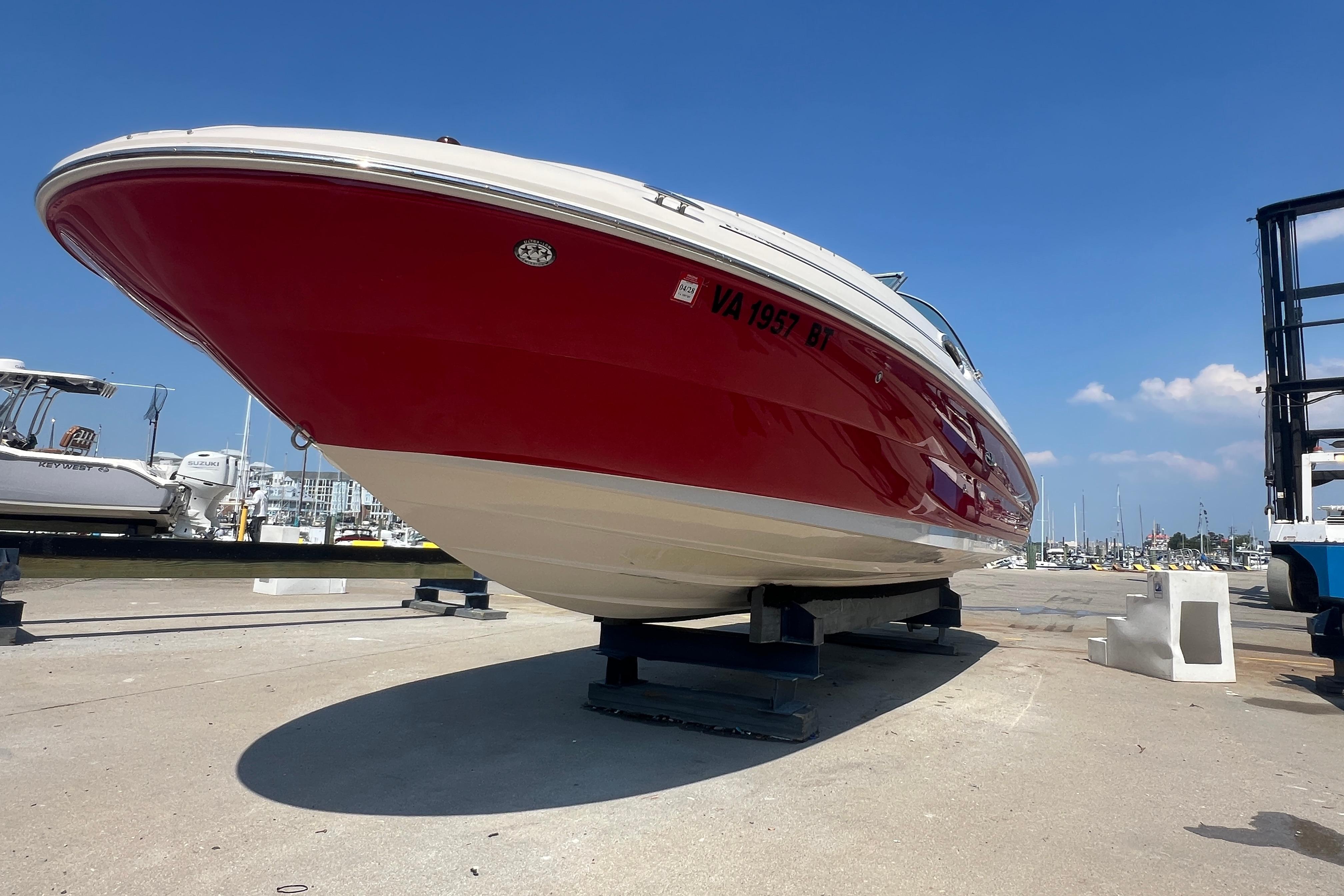 2005 Sea Ray 240 Sundeck boat with red hull on dry dock under clear blue sky.