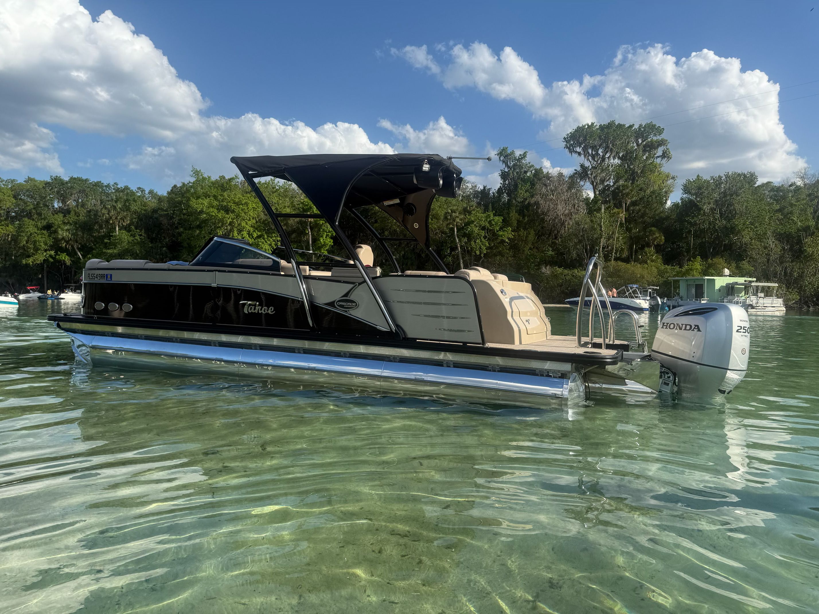 A sleek pontoon boat with a black canopy on clear water.