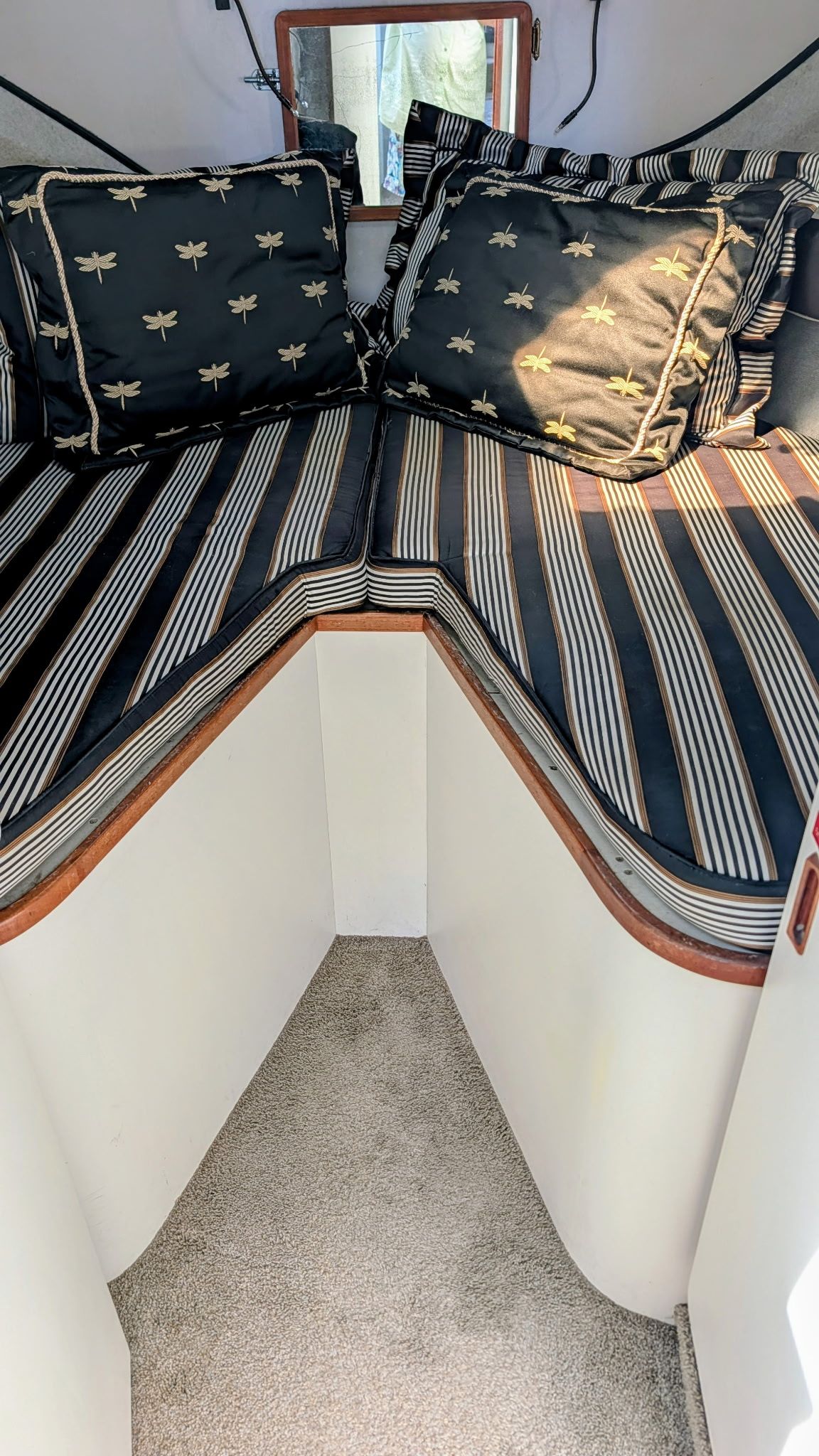 Cabin with striped bedding and dragonfly-patterned pillows, carpeted floor, and wooden accents.