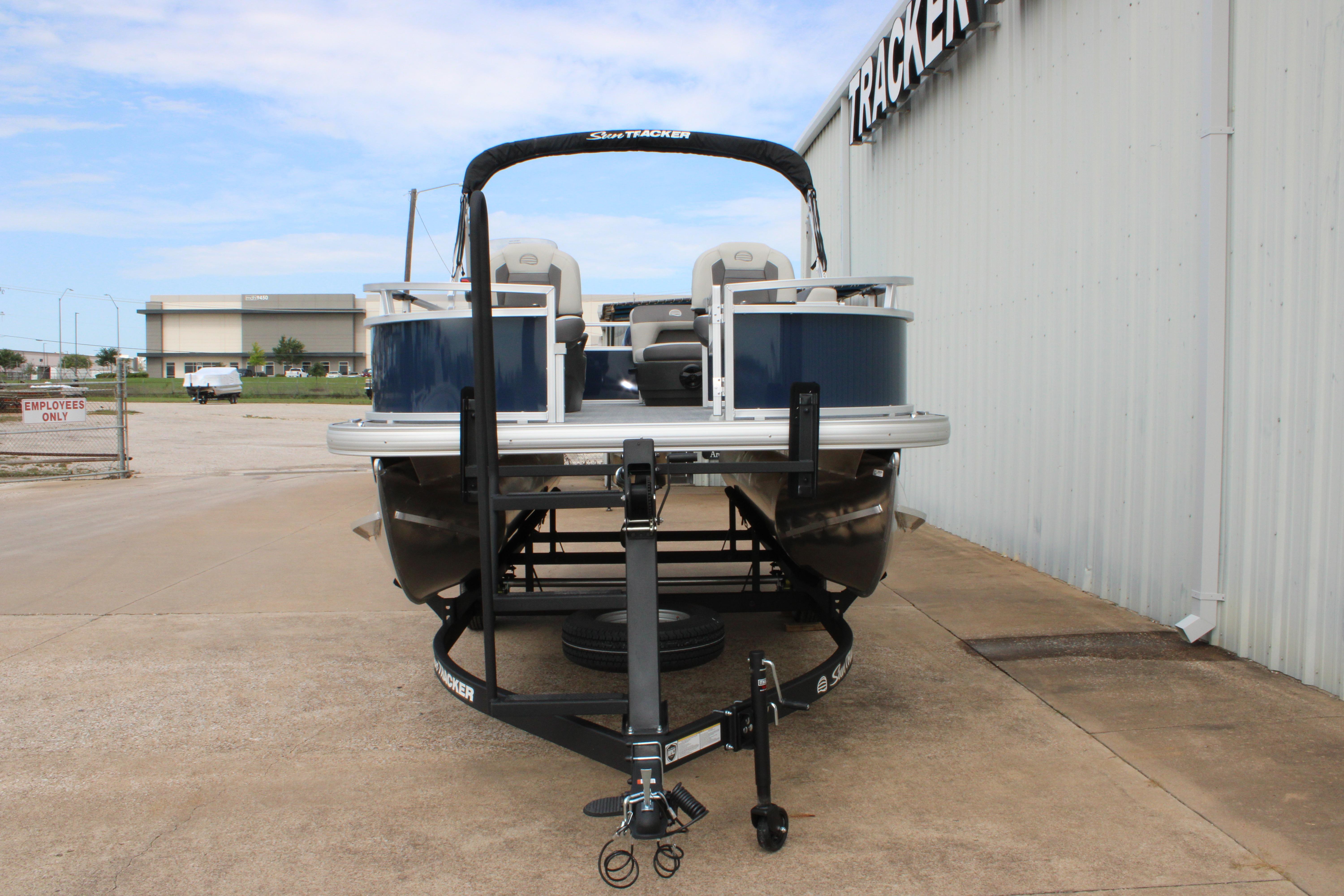 2026 Sun Tracker Bass Buggy 16 XL Select pontoon boat on trailer, parked outside dealership.