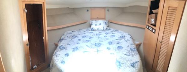 1997 Bertram Convertible boat cabin with a cozy bed and wooden storage cabinets.