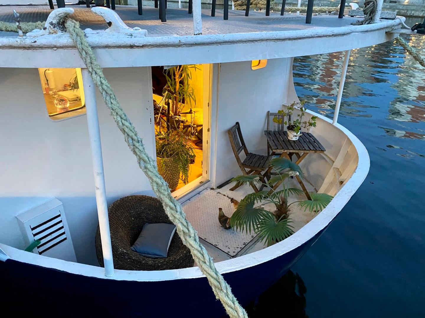 Classic 1896 icebreaker boat with cozy deck, plants, and seating area by the water.