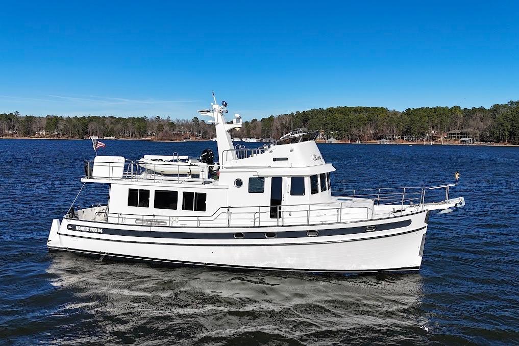 2007 Nordic Tug 54 cruising on a serene lake under a clear blue sky.