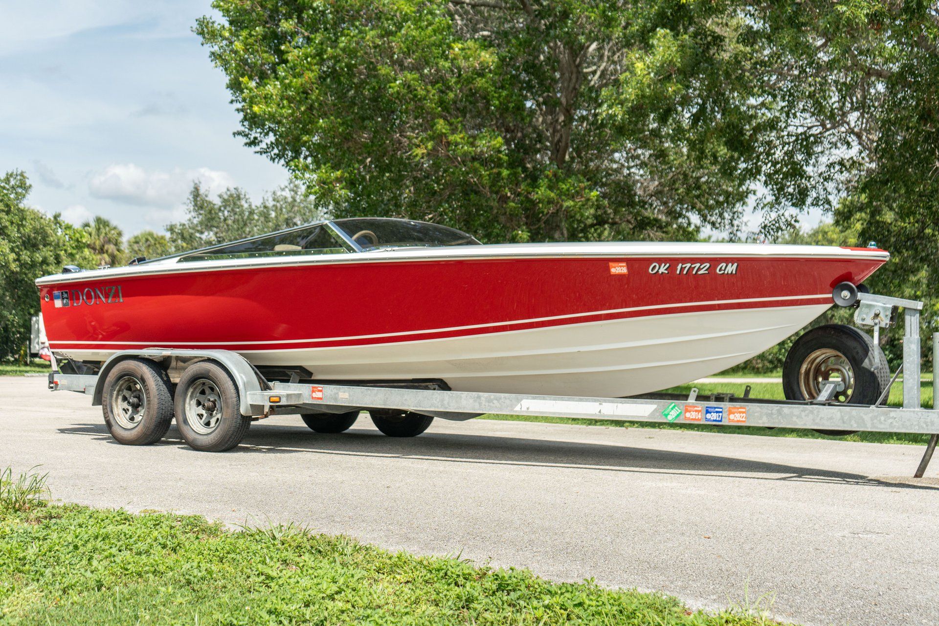 A red 1995 Donzi Classic boat on a trailer, surrounded by trees.