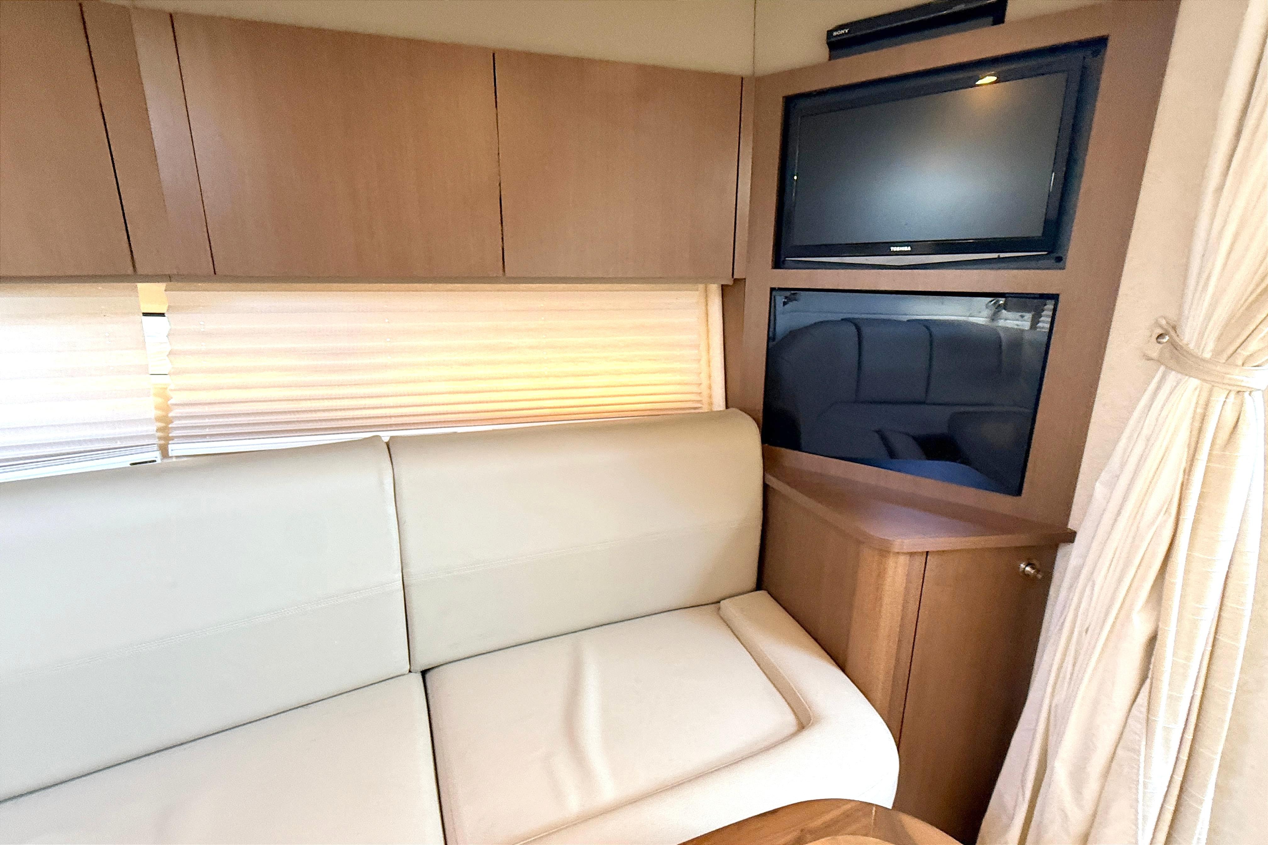 Interior of 2013 Sea Ray 370 Venture with TV, beige sofa, and wooden cabinetry.