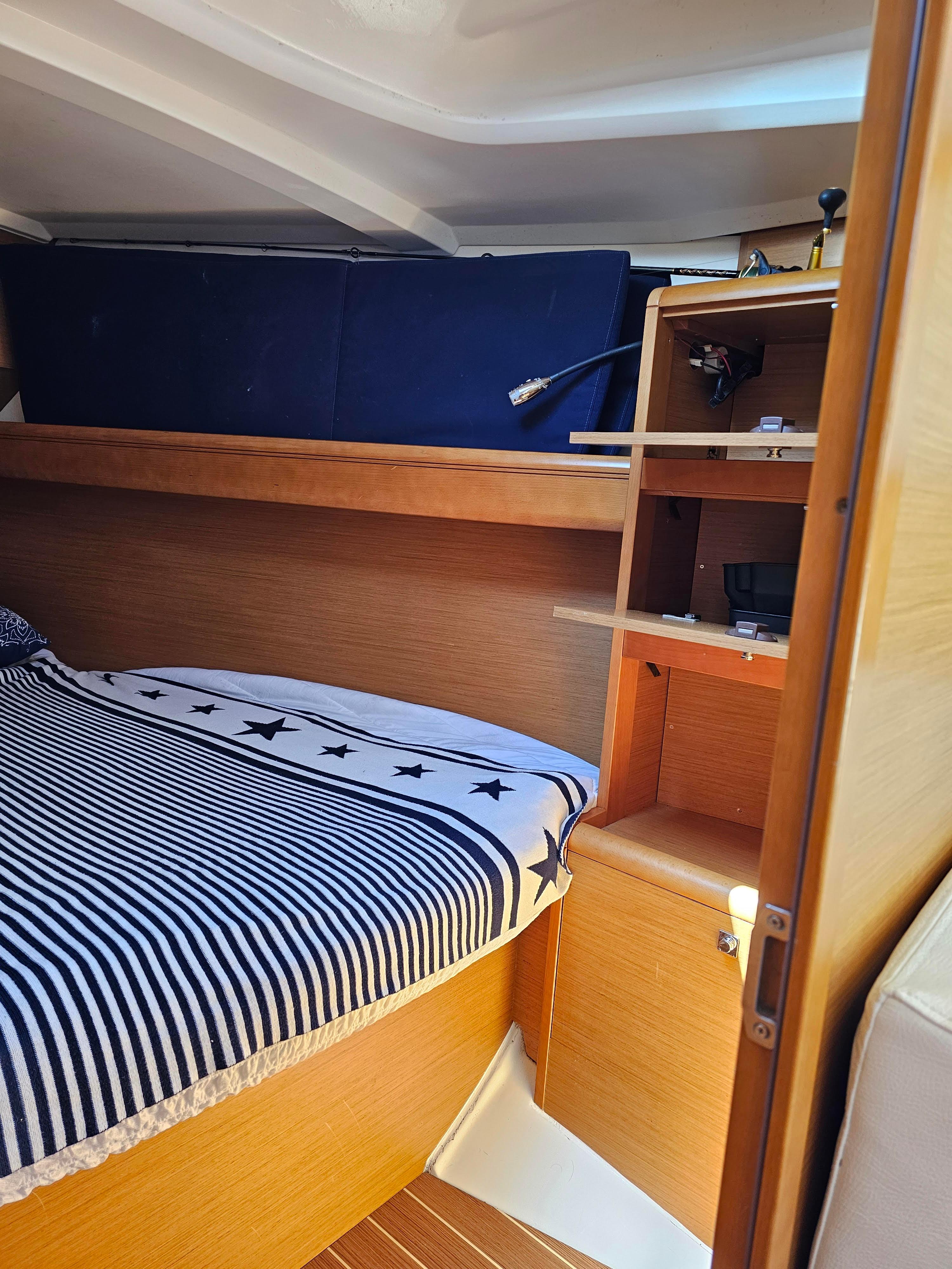 2016 Jeanneau 379 cabin interior with striped bedding and wooden shelves.