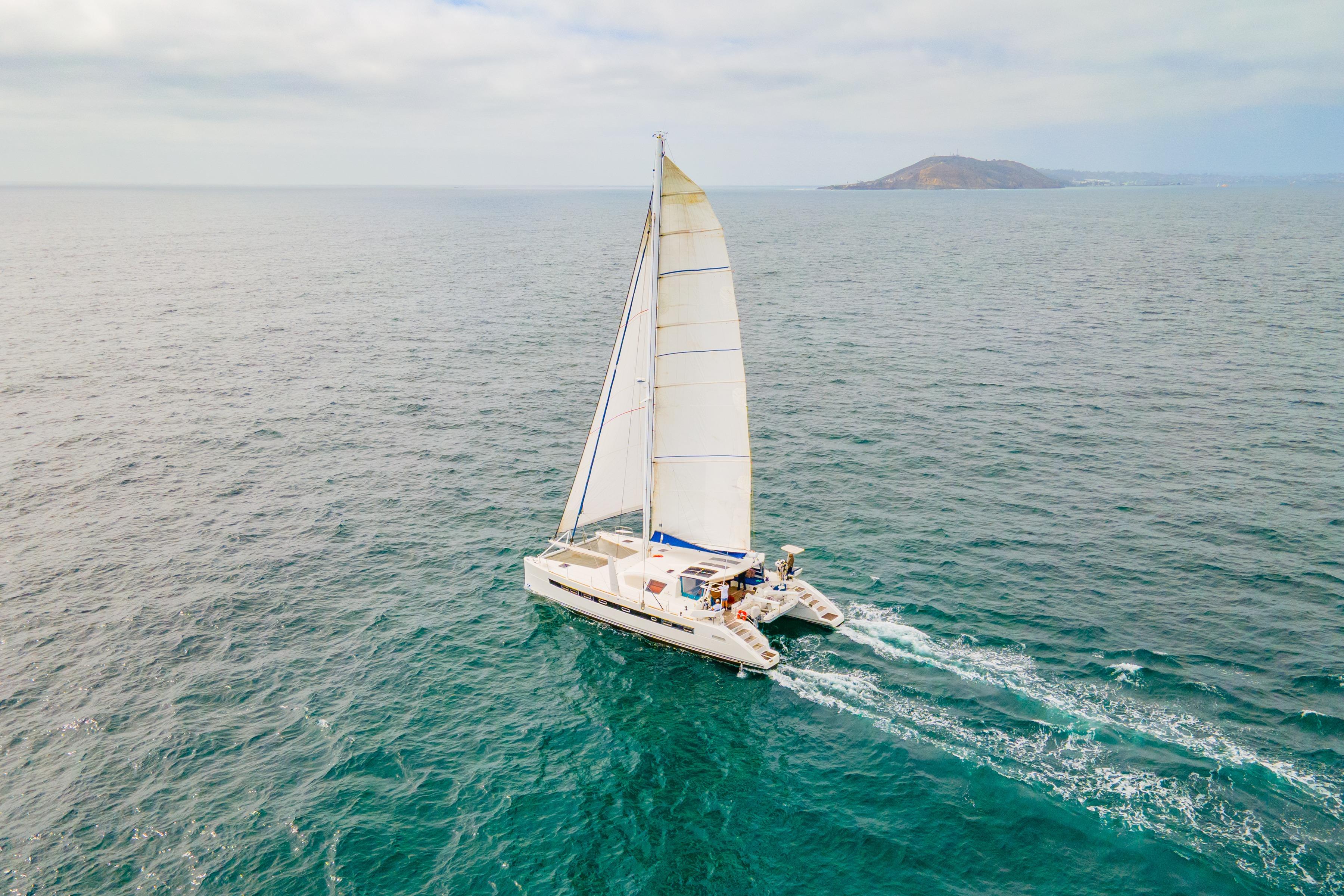 2009 Catana 65 sailing catamaran cruising on open sea with distant island view.