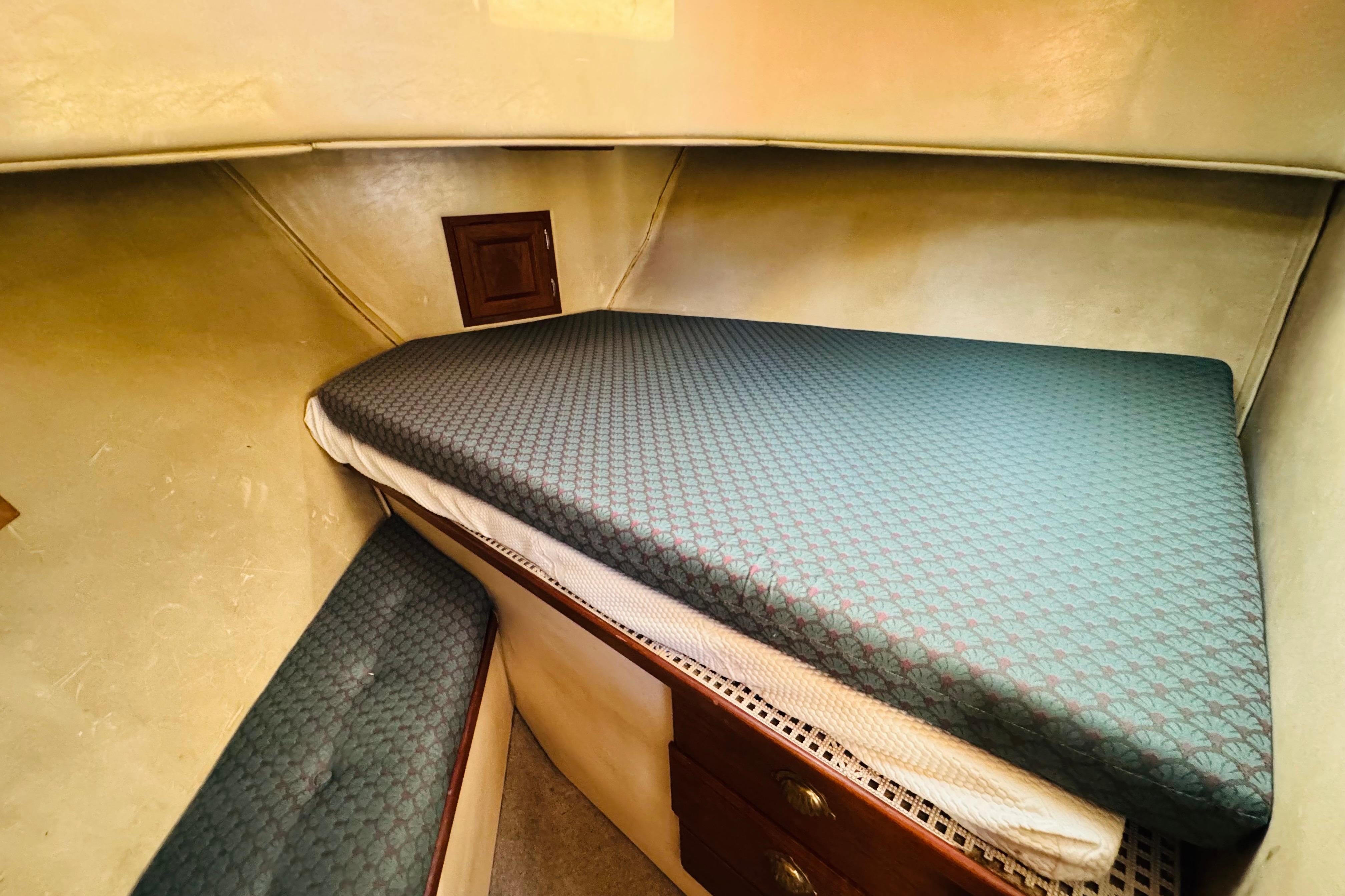 Cozy cabin interior of 1996 Nordic Tug 32 with patterned bedding and wooden storage.