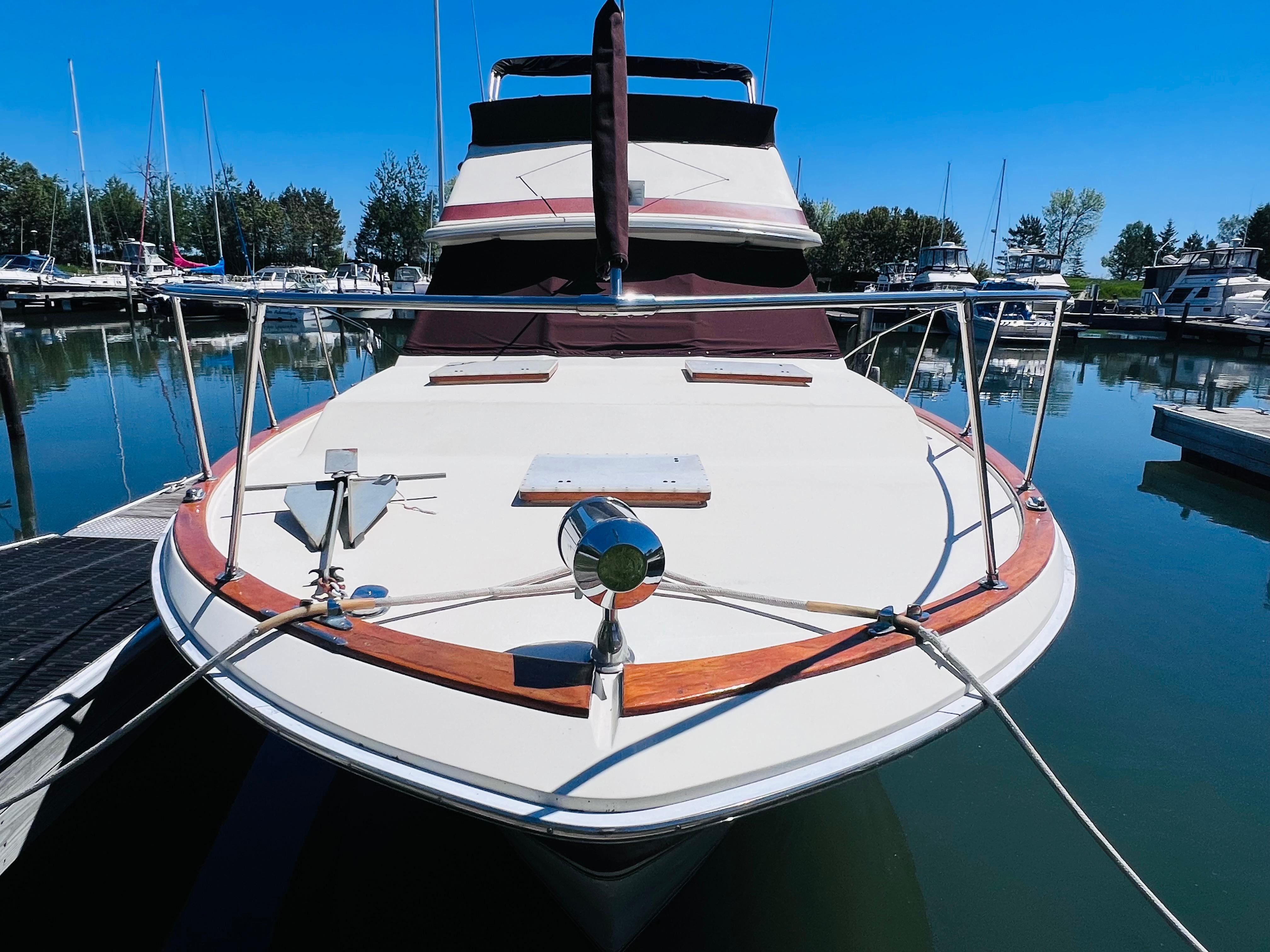 1982 Trojan F32 boat docked in a marina, clear blue sky, calm water.