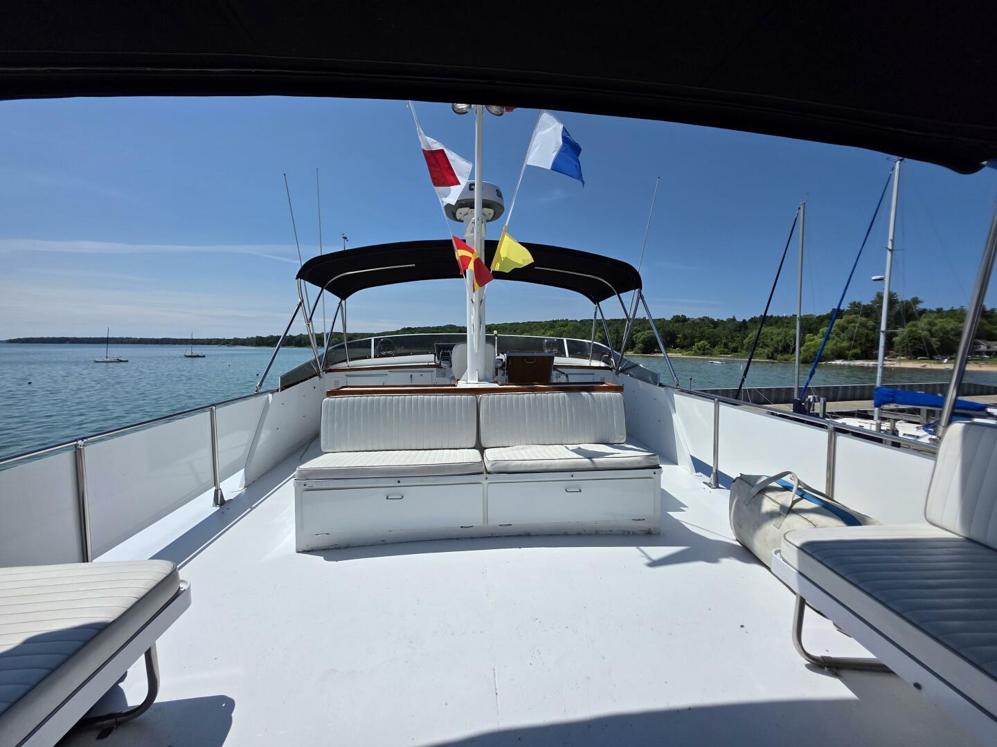 1976 Chris-Craft Roamer 60 yacht deck with seating, flags, and scenic water view.