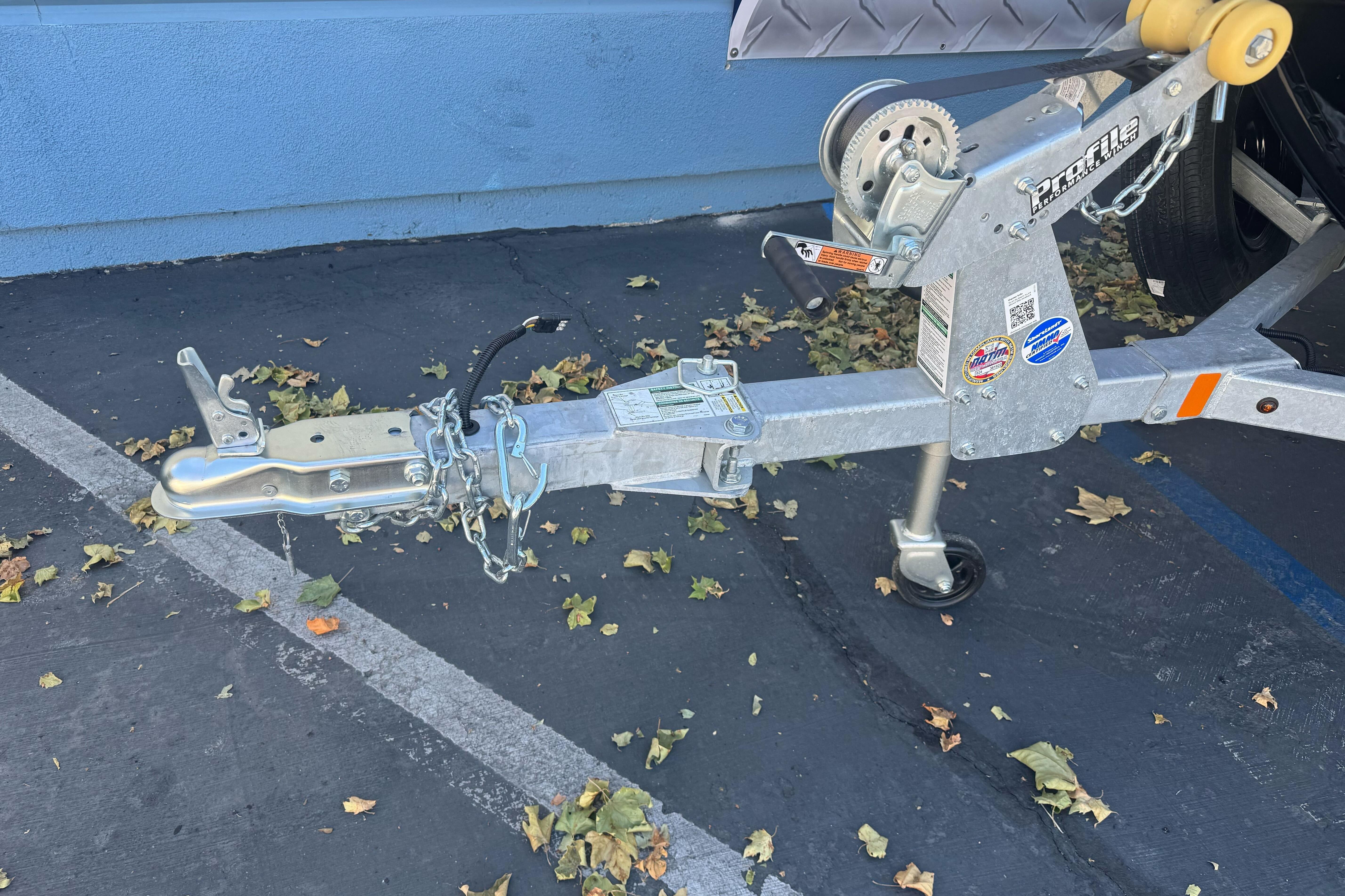 Trailer hitch of a 2026 Lund 1650 Rebel XL SS boat, parked on asphalt with fallen leaves.