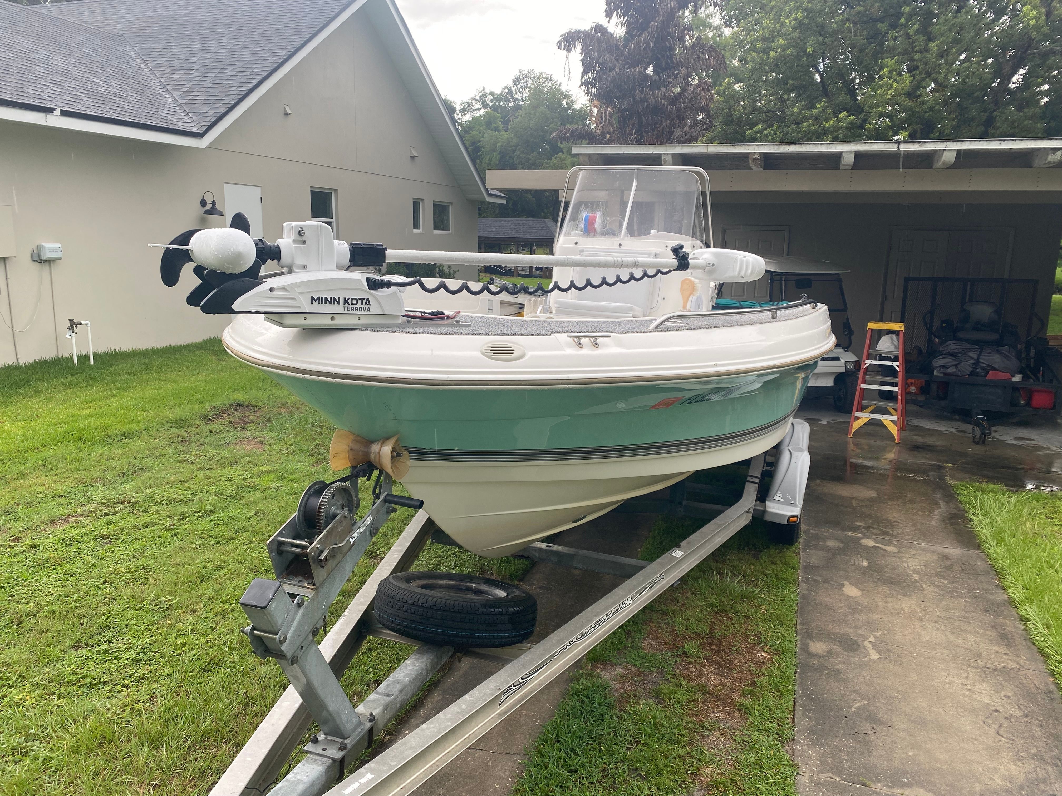 A 2003 Aquasport 201 Osprey boat on a trailer in a yard.