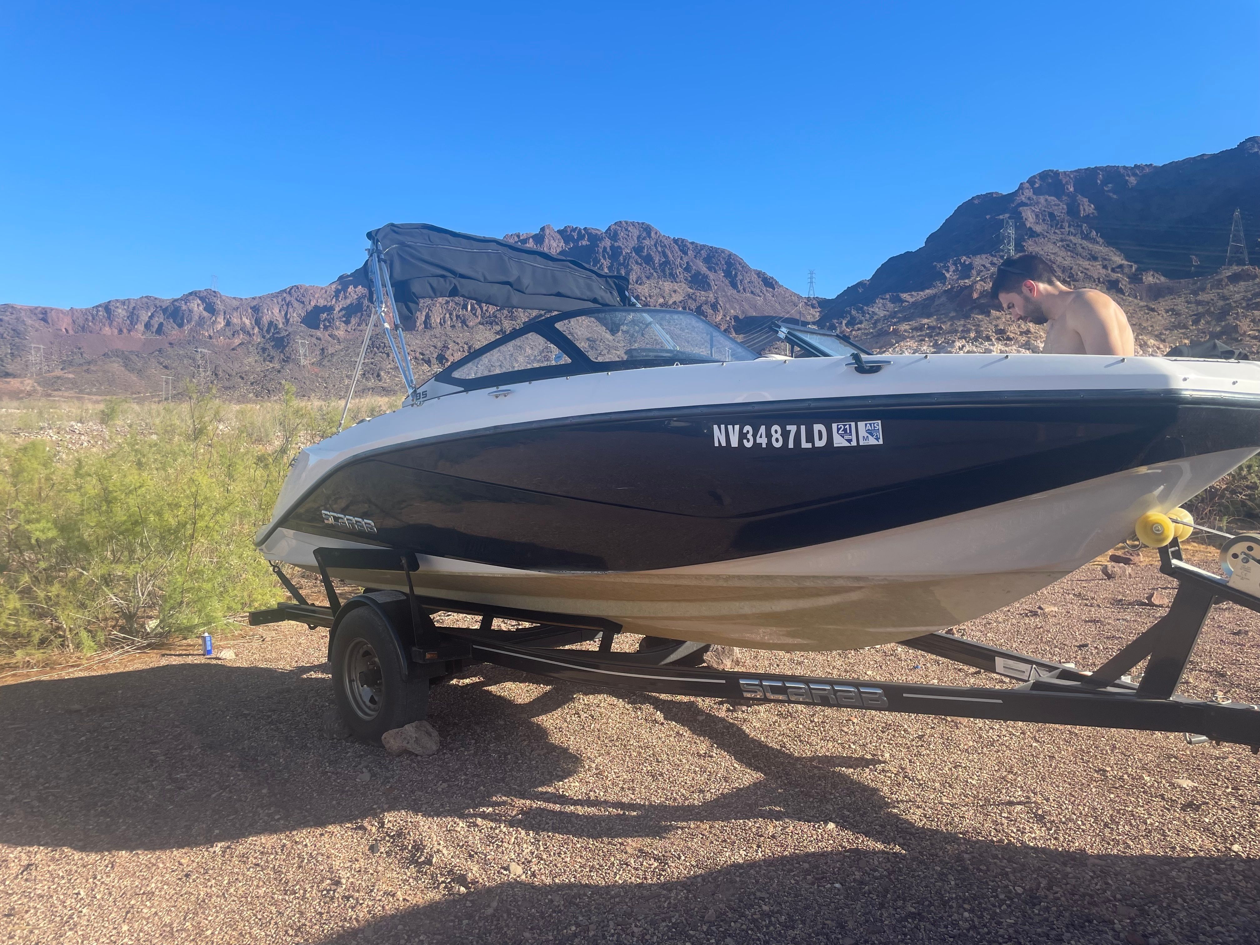 A 2019 Scarab 195 G boat on a trailer in a dry, rocky landscape.