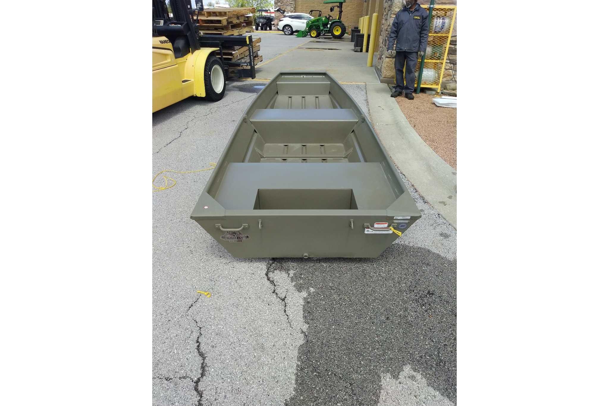2026 Tracker Grizzly 14 Jon boat on pavement, near industrial equipment.