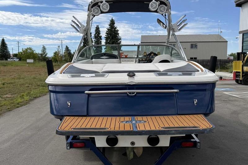 2004 MasterCraft XStar boat with blue hull and teak swim platform, parked outdoors.