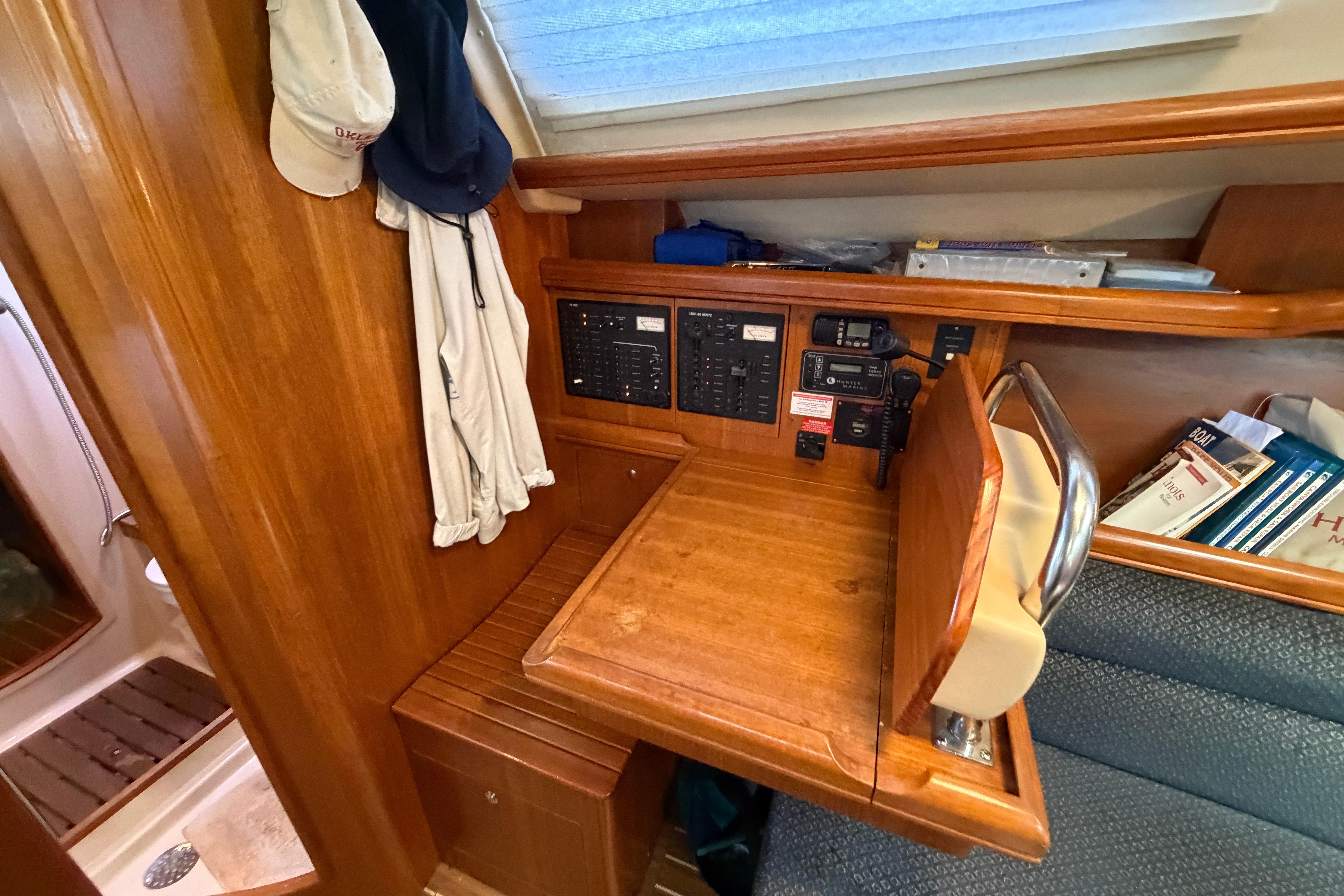 Navigation station inside a 2005 Hunter 38 sailboat with wooden desk and control panels.