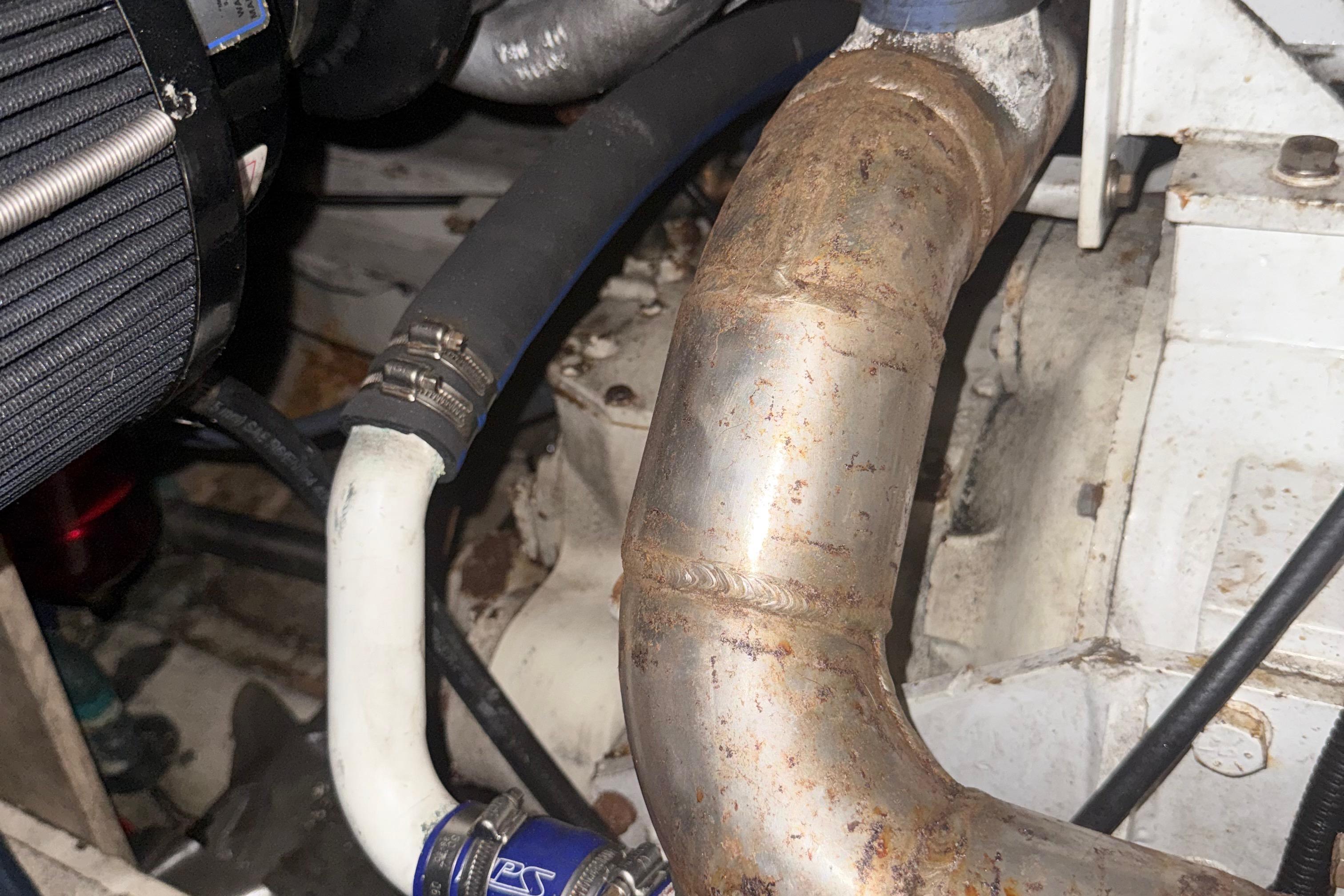 Engine components of a 1974 Pacemaker 48 Sportfisherman boat, featuring hoses and metal pipes.