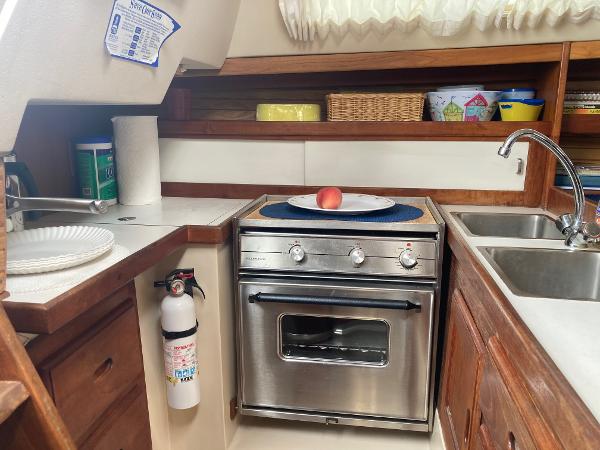 Compact kitchen in a 1989 Catalina 30 sailboat with stove, sink, and storage.