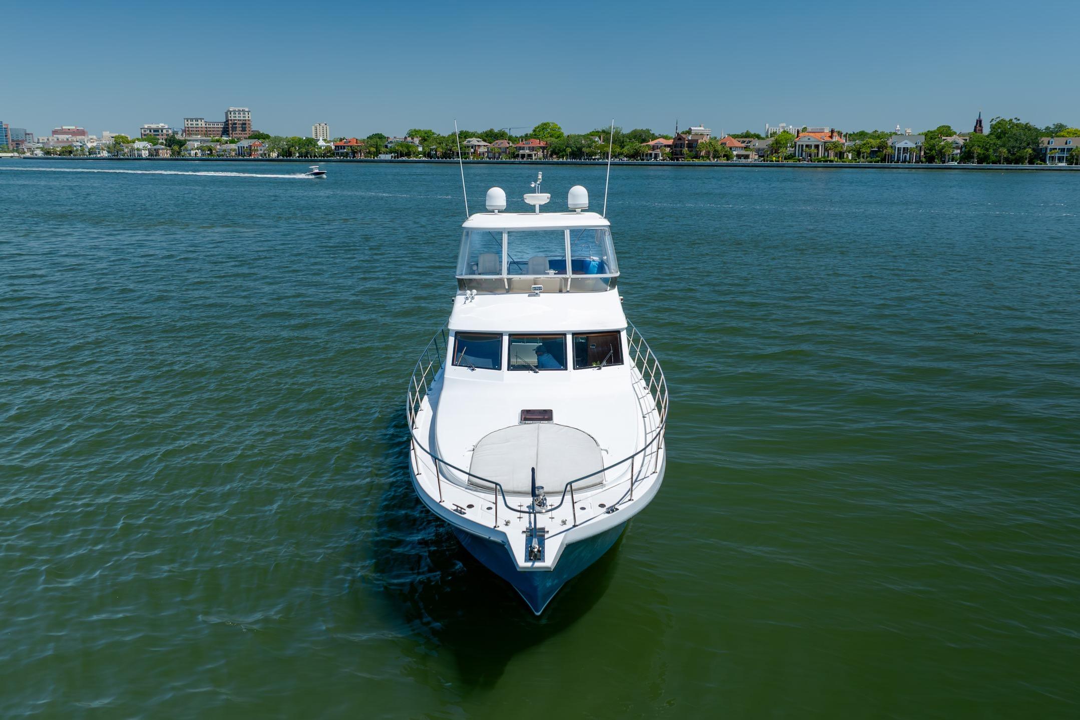 Ocean Alexander yacht cruising on calm waters near a city shoreline.