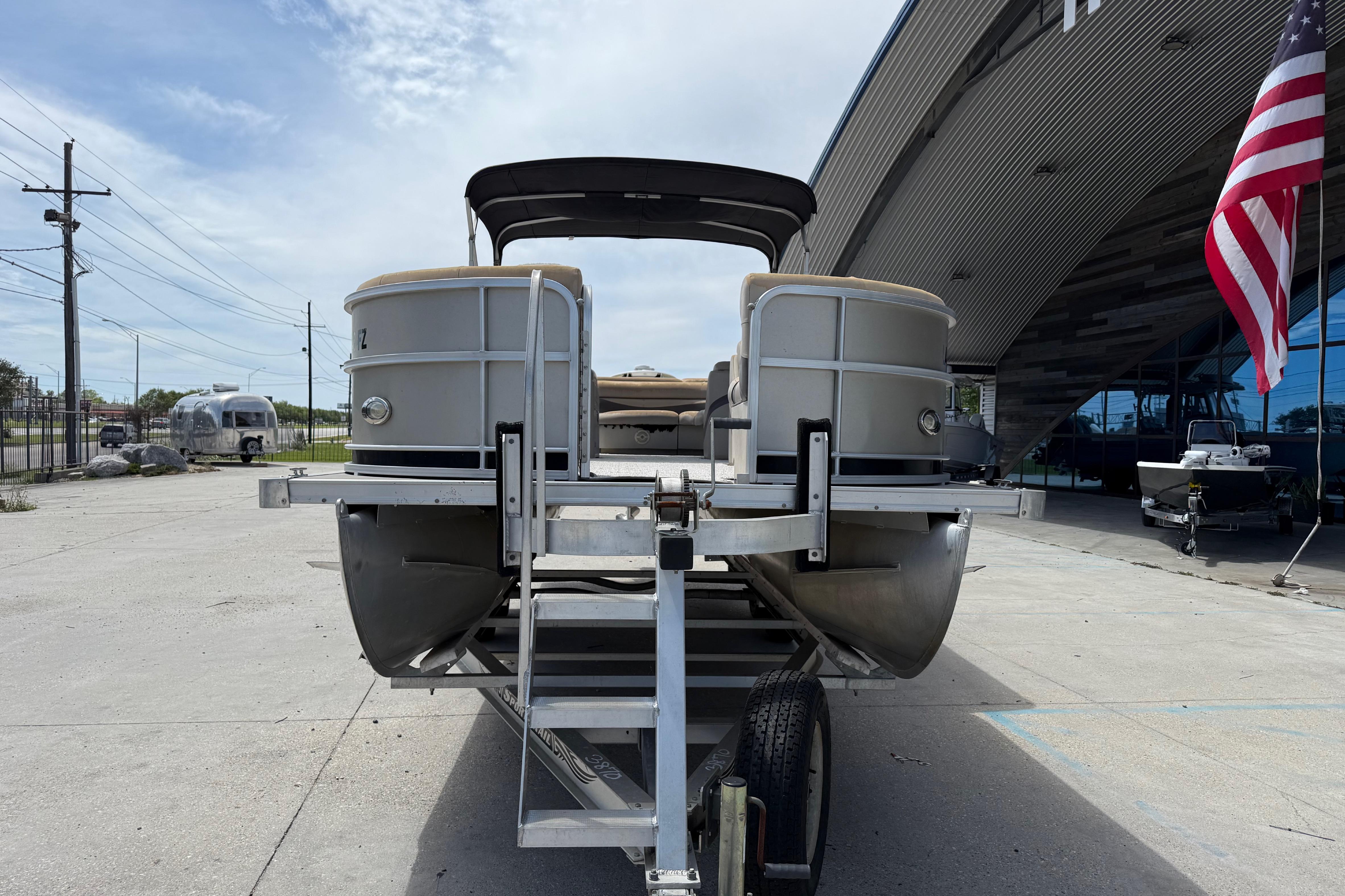 2012 South Bay 522 CR pontoon boat on trailer, parked near modern building and American flag.