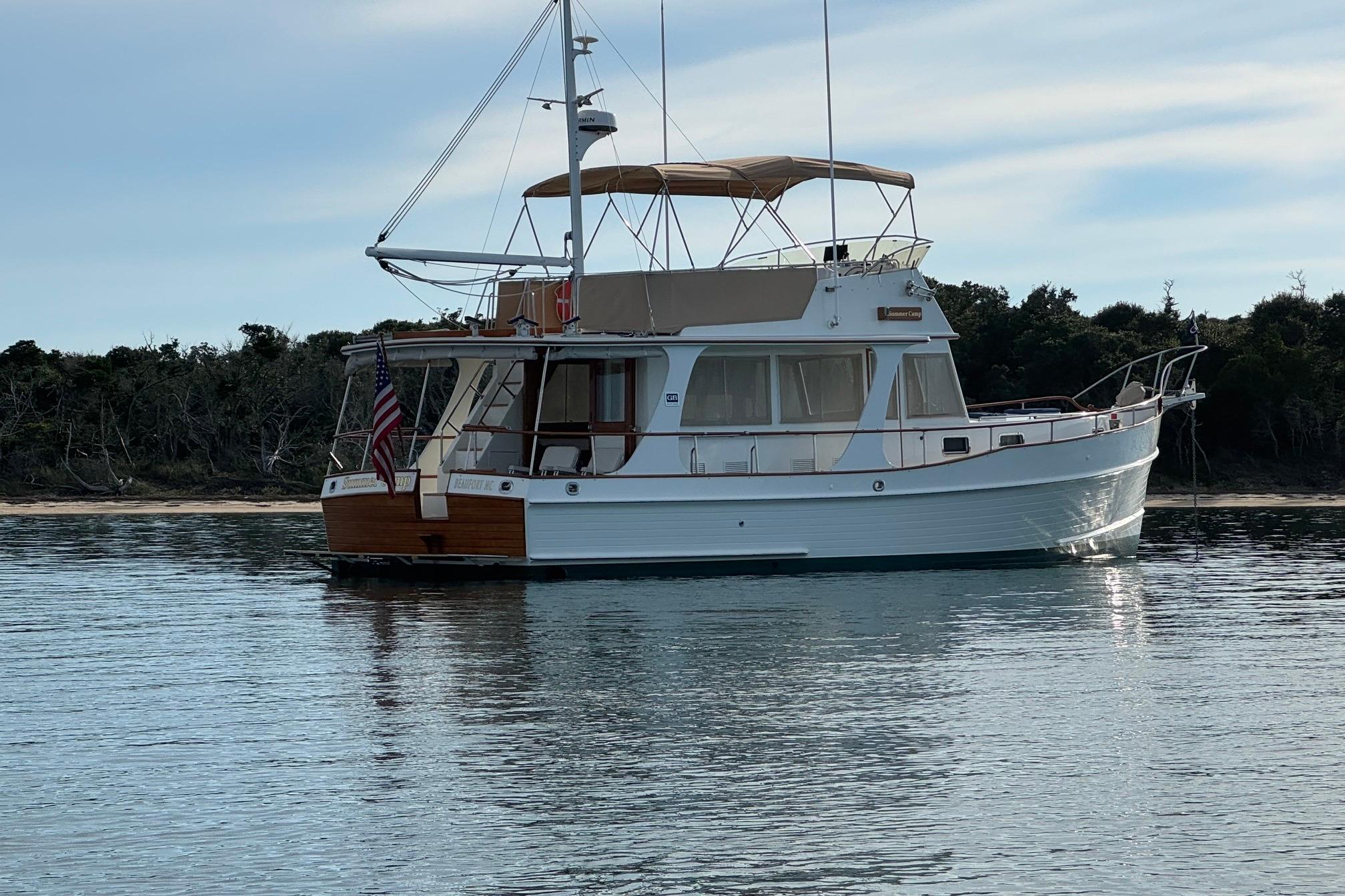 1999 Grand Banks 42 Europa yacht anchored on calm water near a wooded shoreline.
