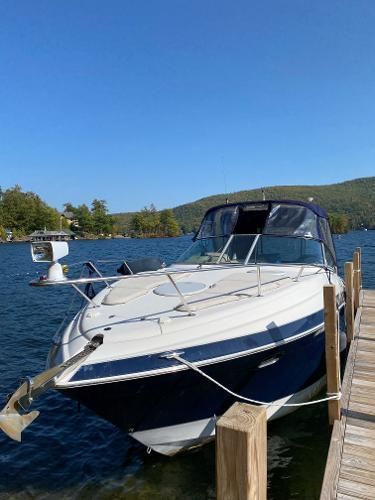 A white and blue boat docked at a wooden pier on a calm lake.