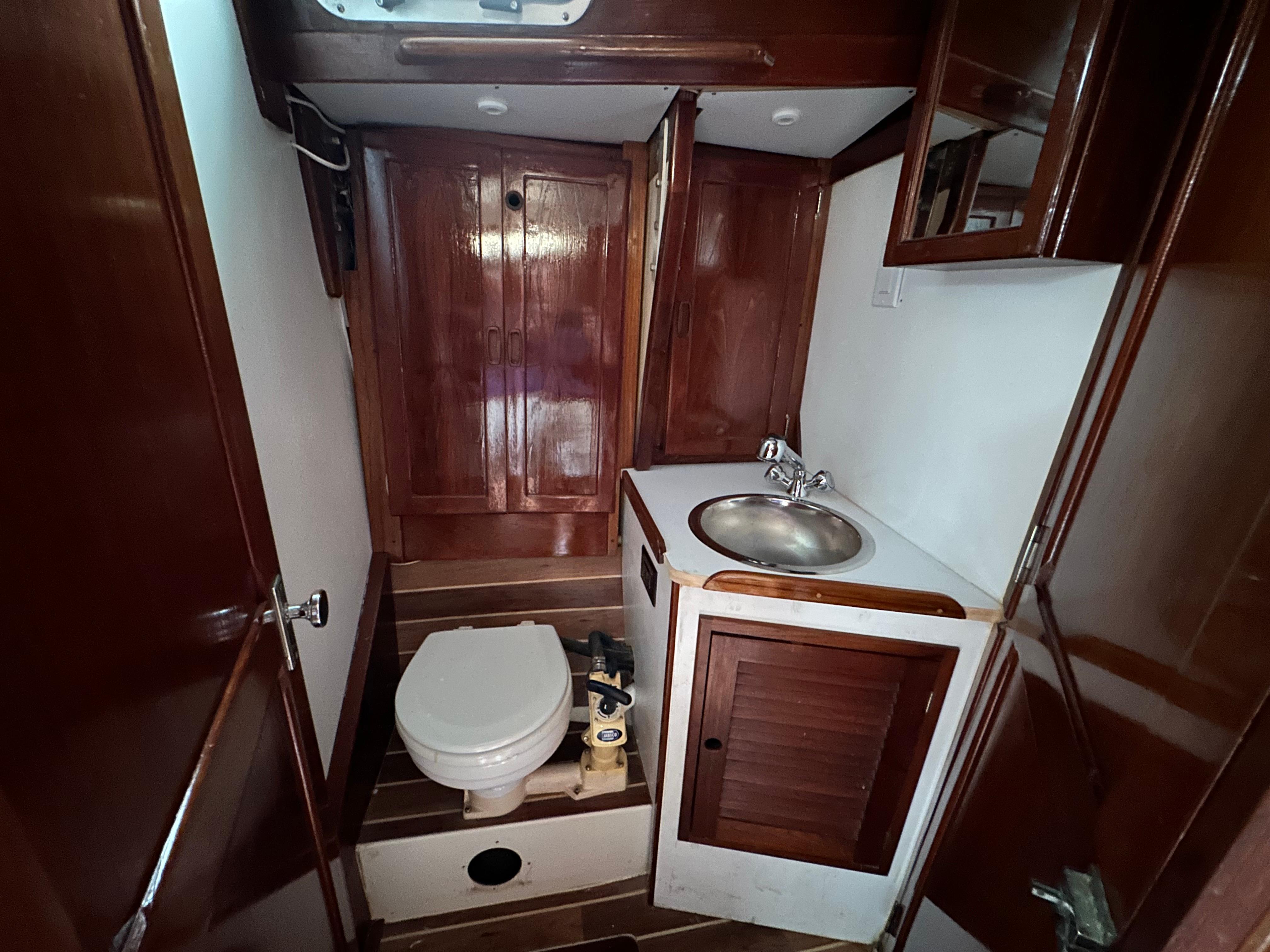 1981 Tartan 37 sloop bathroom with wooden cabinetry, sink, and toilet.