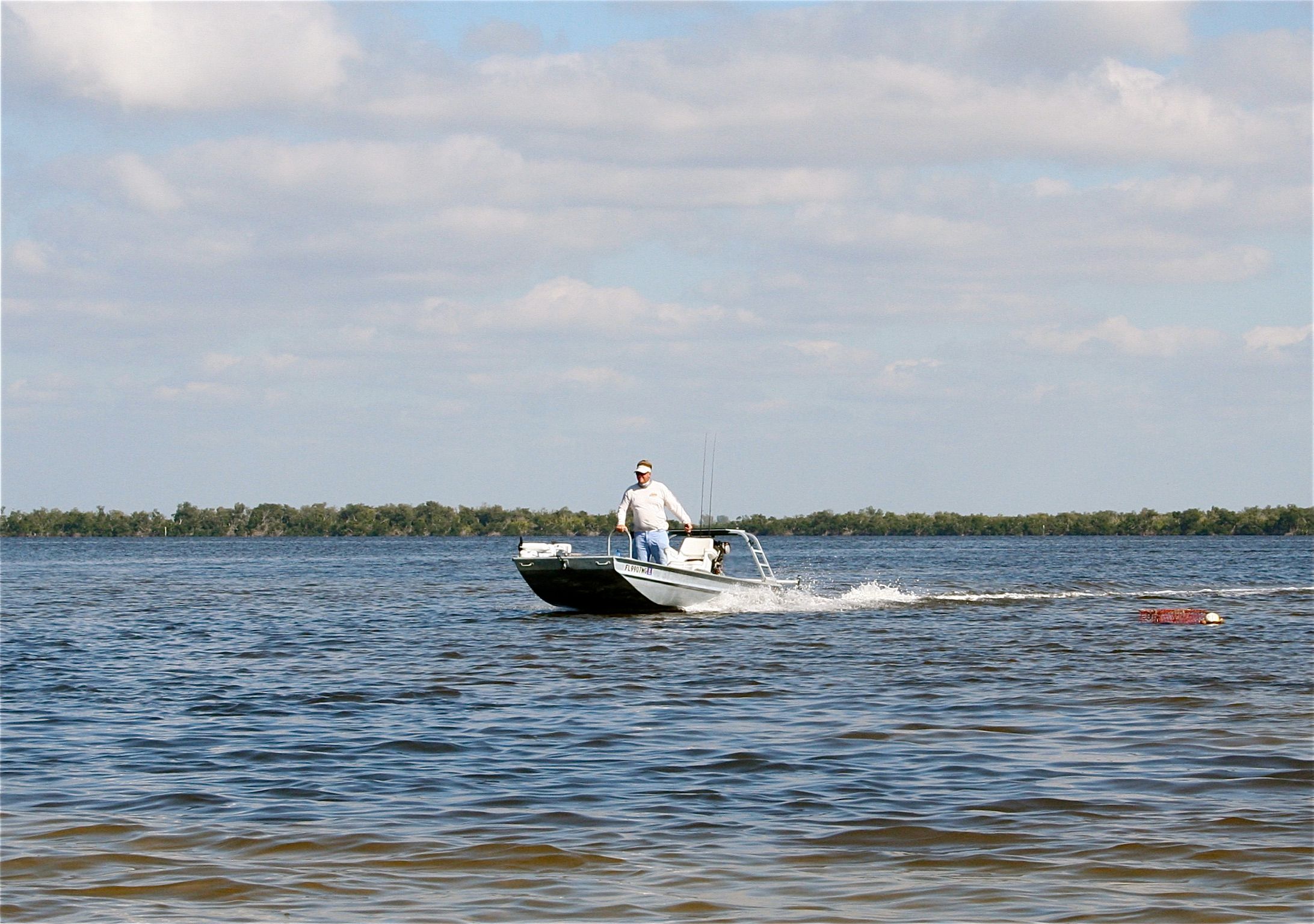 A man operates a small motorboat on calm waters under a cloudy sky.
